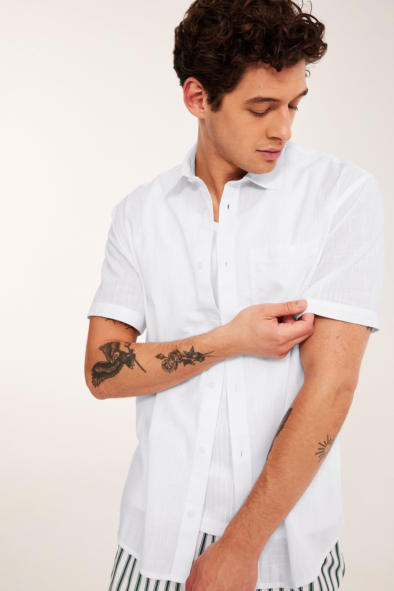 Mies käärii valkoisen kuvioidun lyhythihaisen paidan hihaa, päällä valkoinen verkkohiha-aluspaidan.