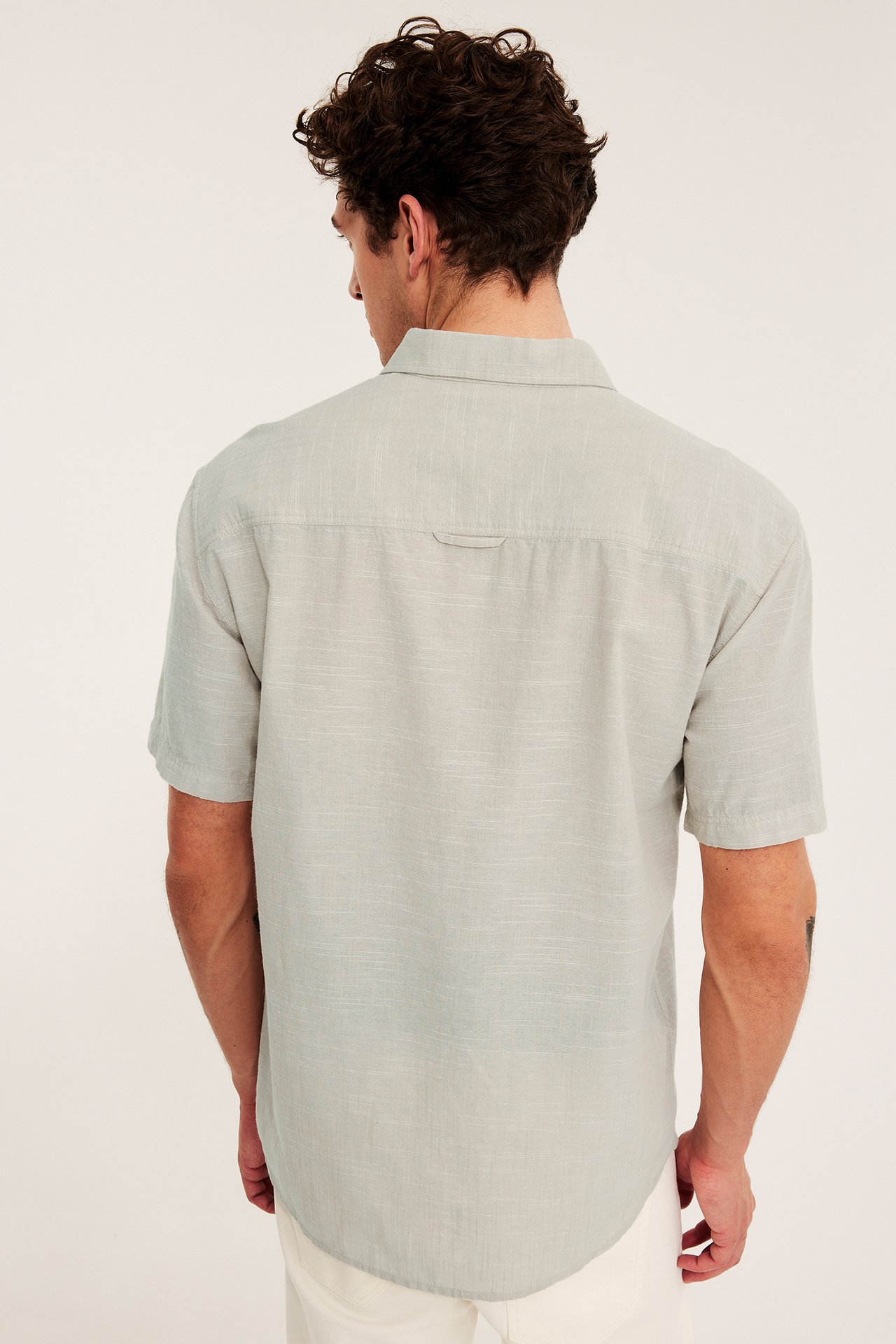 Mies selin, yllään vaaleanbeige regular fit lyhythihainen strukturoitu paita ja vaaleat housut.