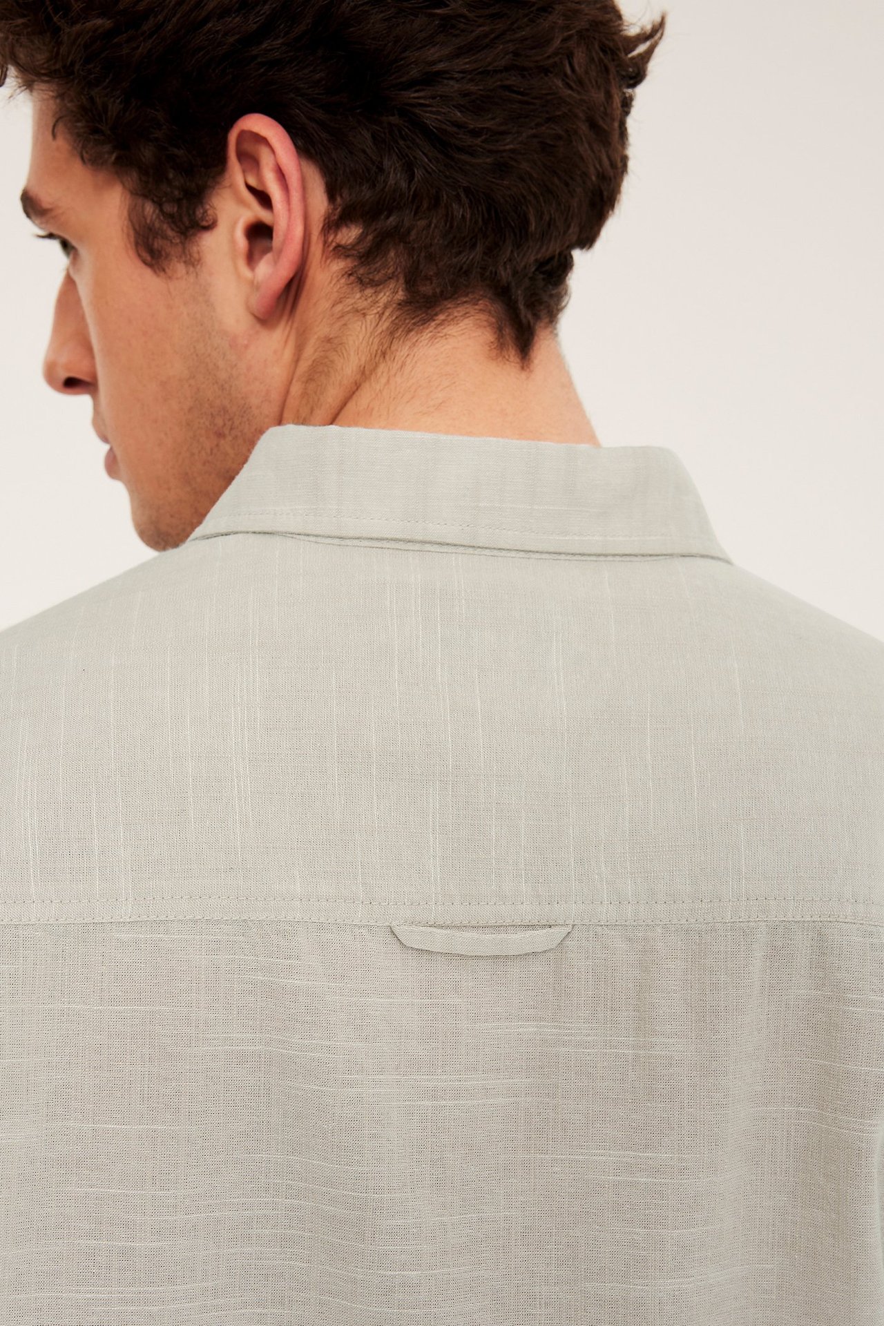 Närbild bakifrån på en man i en beige kortärmad skjorta med normal passform och strukturmönster.