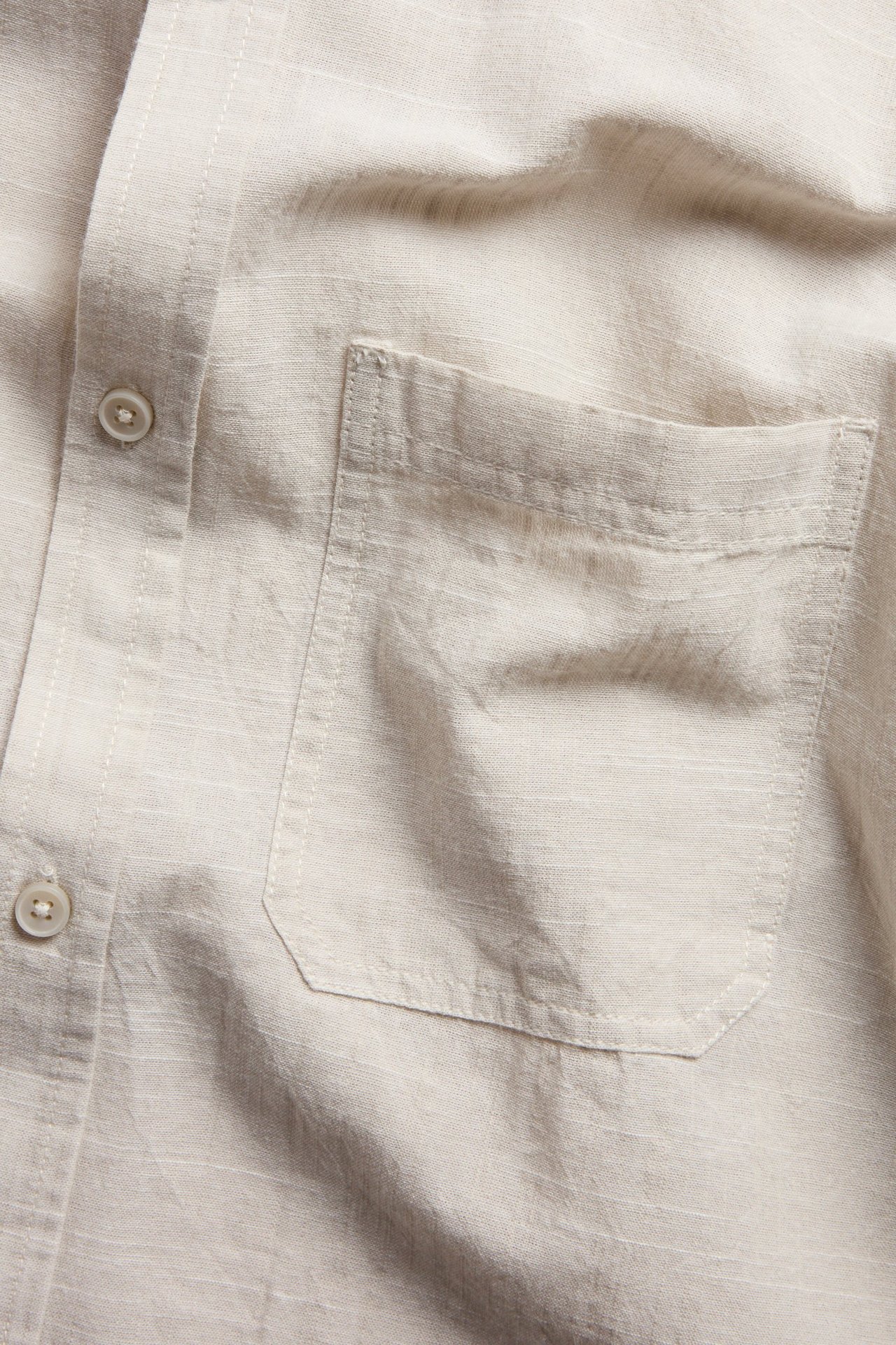 Nærbilde av en beige kortermet herreskjorte i regular fit med strukturert stoff, brystlomme og knapper.