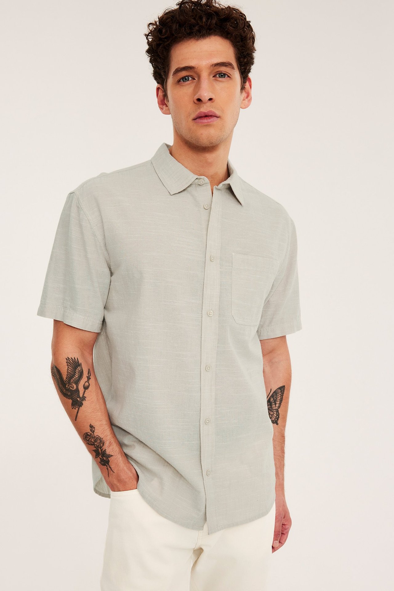 Edestäpäin mies yllään vaaleabeige lyhythihainen paita rintataskulla ja vaaleat housut.