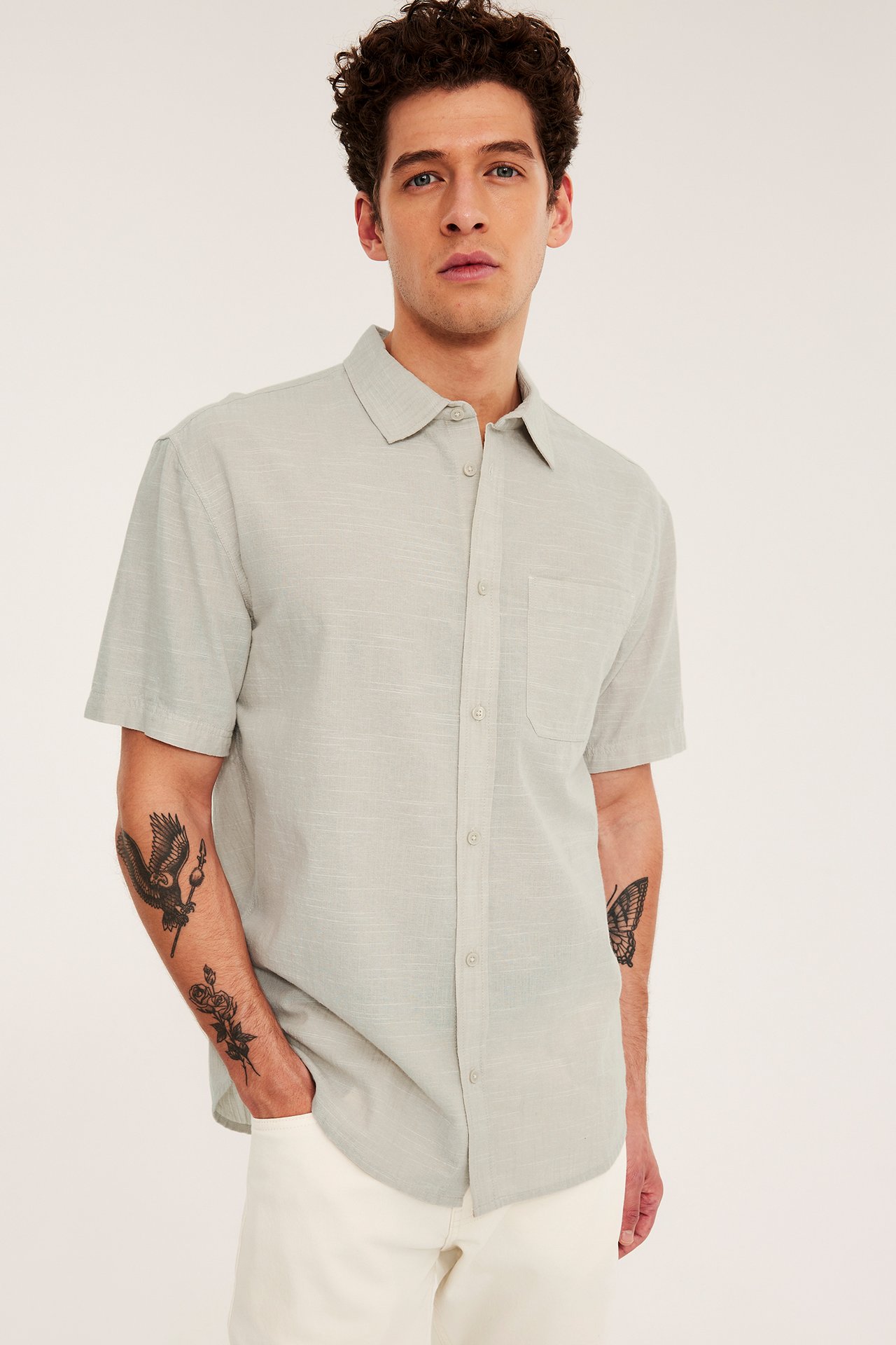 Edestäpäin mies yllään vaaleabeige lyhythihainen paita rintataskulla ja vaaleat housut.