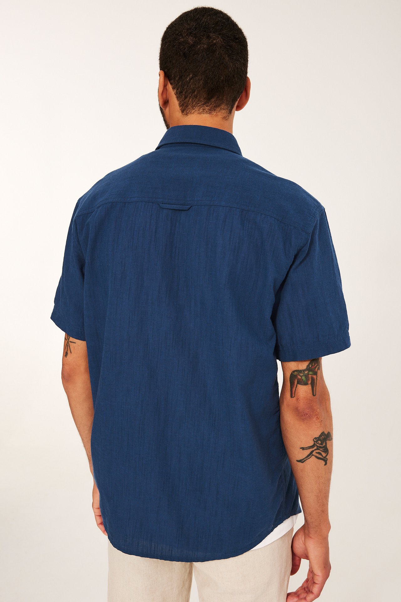 Ryggvy av en man i en blå strukturerad kortärmad skjorta, vit t-shirt och beiga byxor.