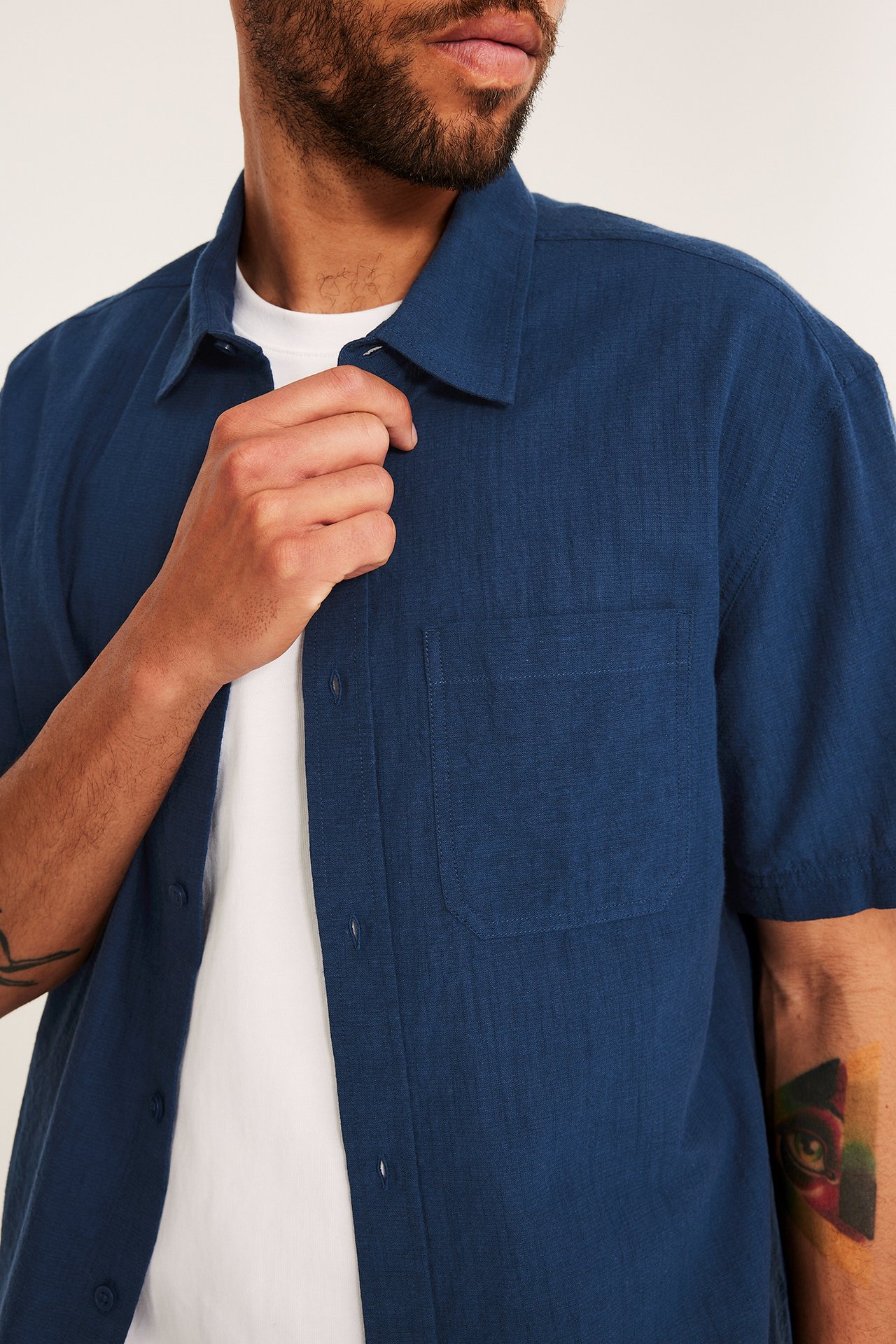 Närbild framifrån på en man i en öppen blå texturerad kortärmad skjorta över en vit t-shirt.