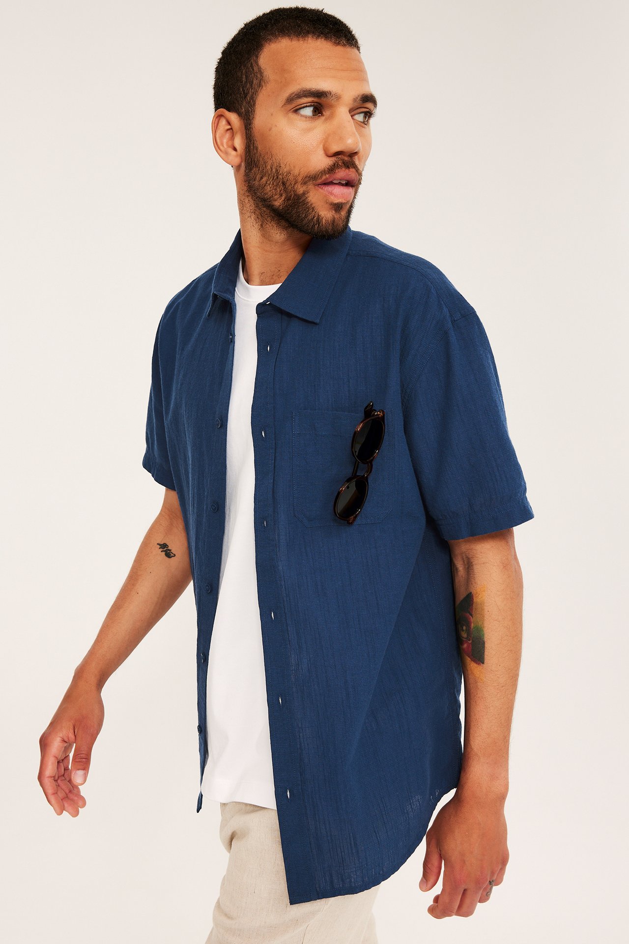 Sidovy av man i öppen blå texturerad kortärmad skjorta över vit t-shirt, med solglasögon.