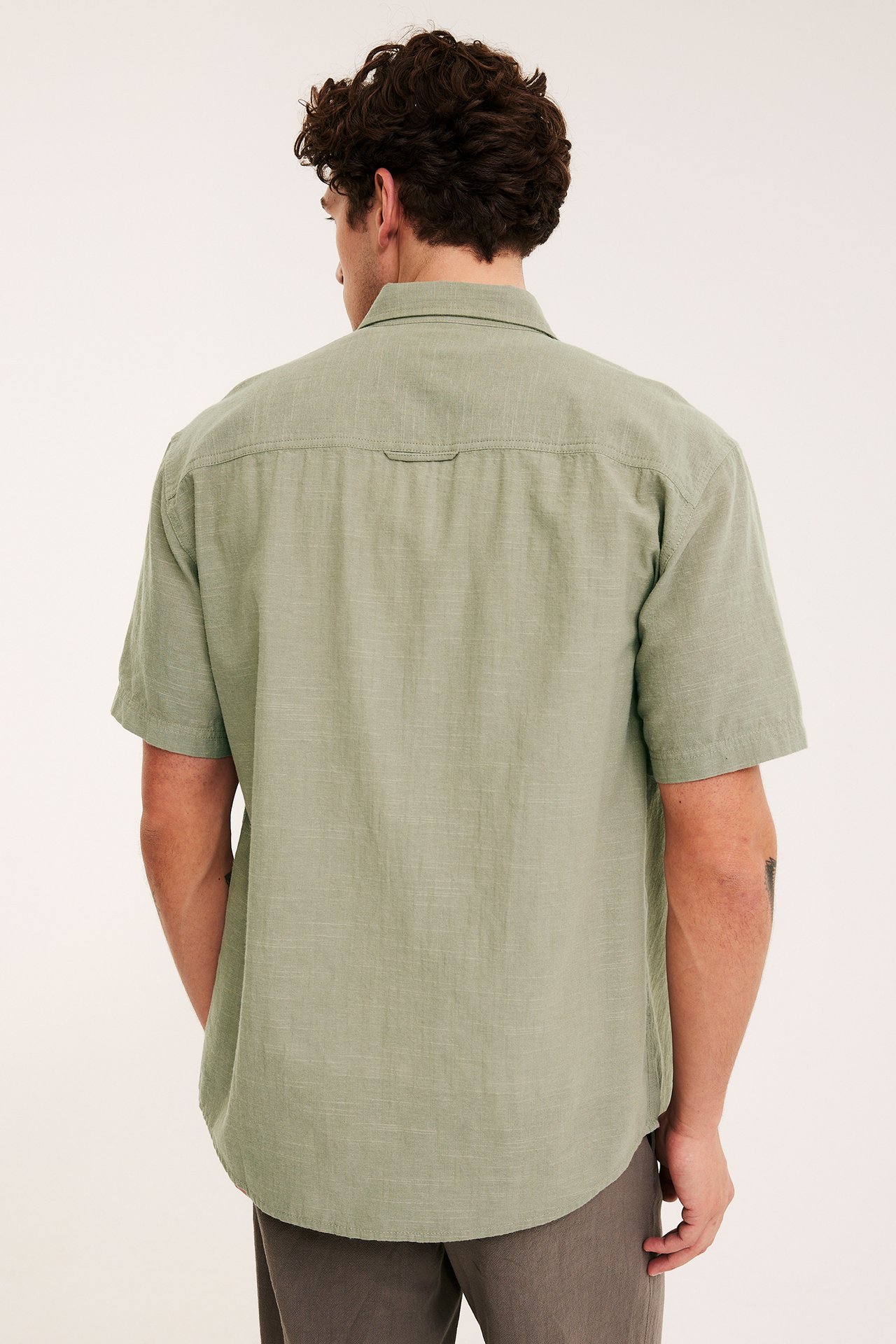 Widok z tyłu mężczyzny w khaki zielonej koszuli z krótkim rękawem regular fit i ciemnych spodniach.