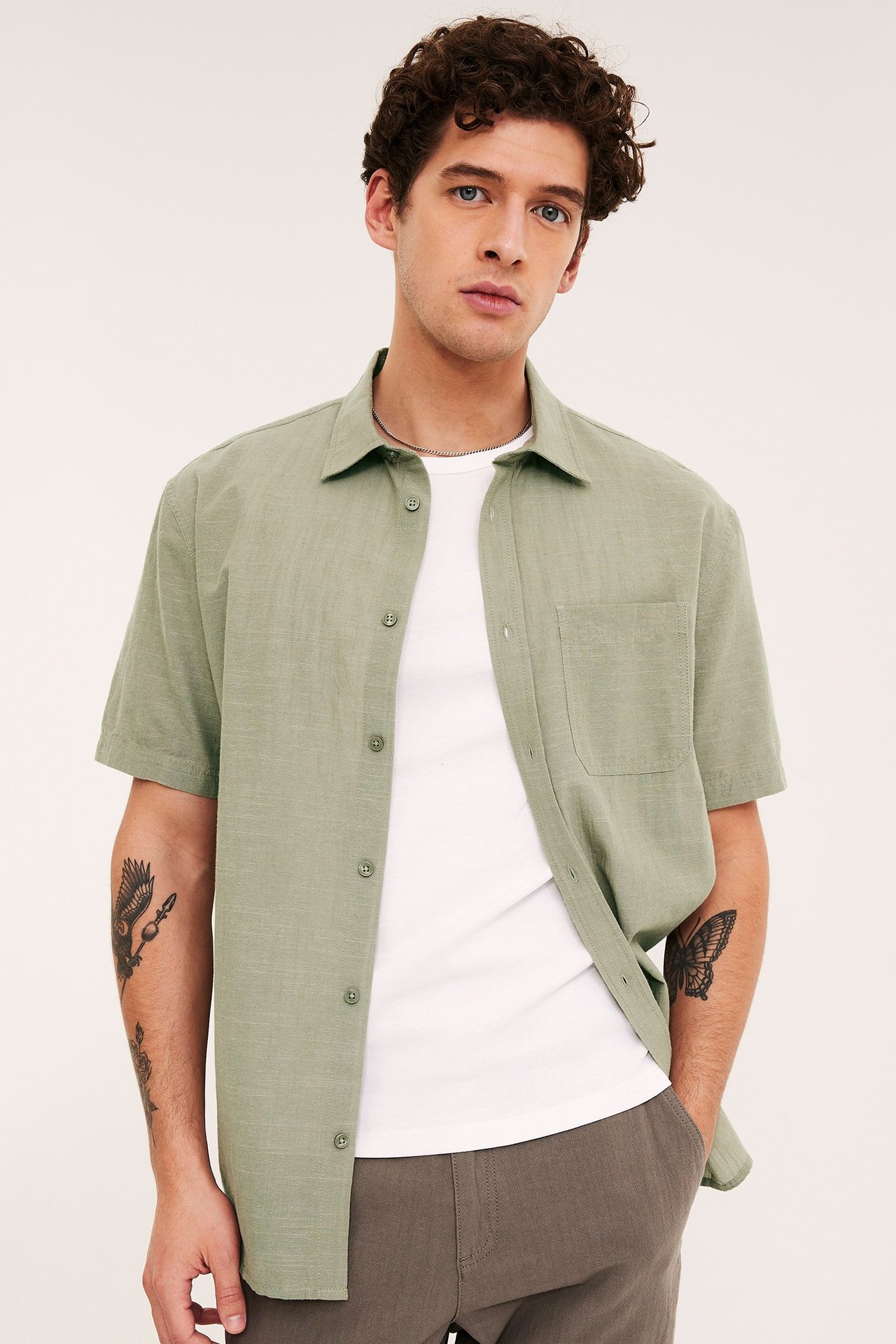 Frontutsikt: Mann i khakigrønn teksturert kortermet skjorte over hvit t-skjorte og mørk bukse.