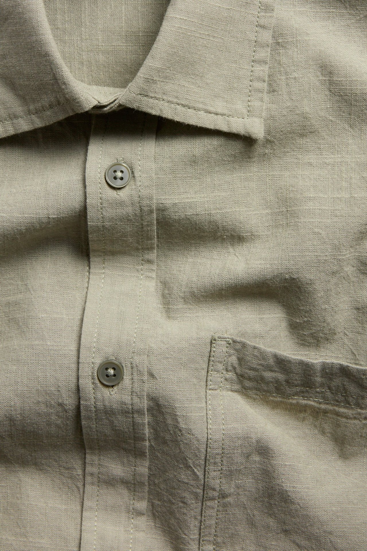 Zbliżenie na khaki zieloną koszulę z krótkim rękawem, teksturowaną, z kołnierzykiem i kieszenią na piersi.