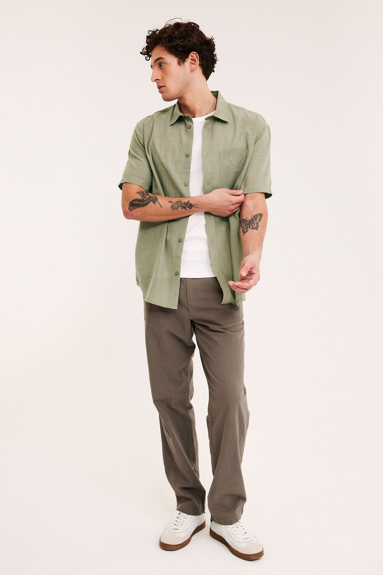 Framsida: man i kaki-grön strukturerad kortärmad skjorta över vit t-shirt, bruna byxor, vita sneakers.