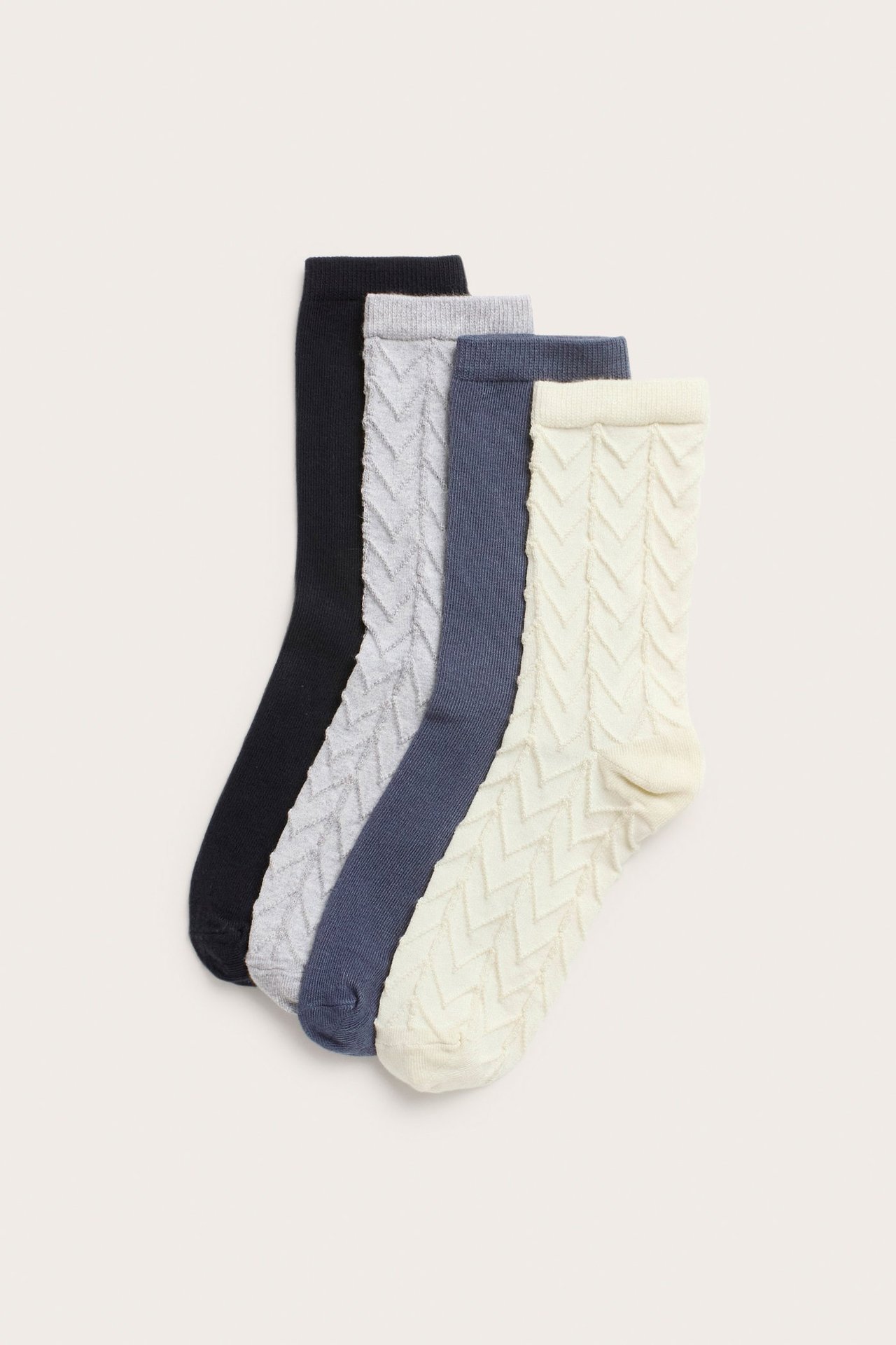 Edestä näkymä neljästä puuvillasekoitesukasta: kermanväriset ja vaaleanharmaat kuvioidut, yksiväriset tummansiniset ja mustat.