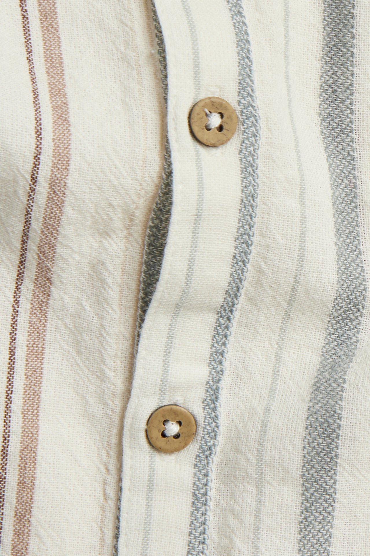 Zbliżenie na pasiasty tkany bawełniany romper w kolorze złamanej bieli z widocznymi drewnianymi guzikami z przodu.