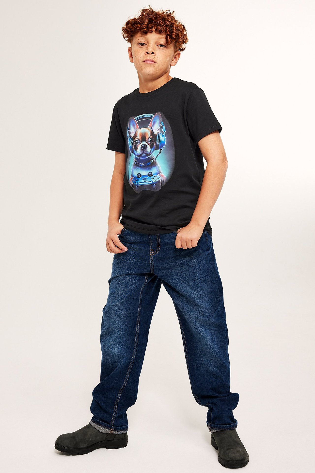 Svart T-shirt med tryck på framsidan, bärs av en pojke, skogahängande jeans och mörk sneakers.