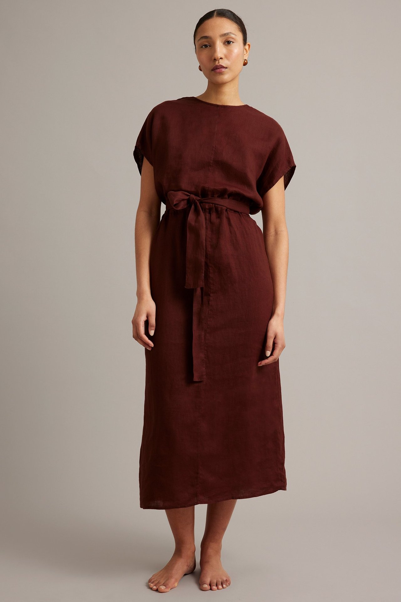 Edestä päin nainen viininpunaisessa pellavaisessa v-aukkomekossa, jossa on vyötärönauha.