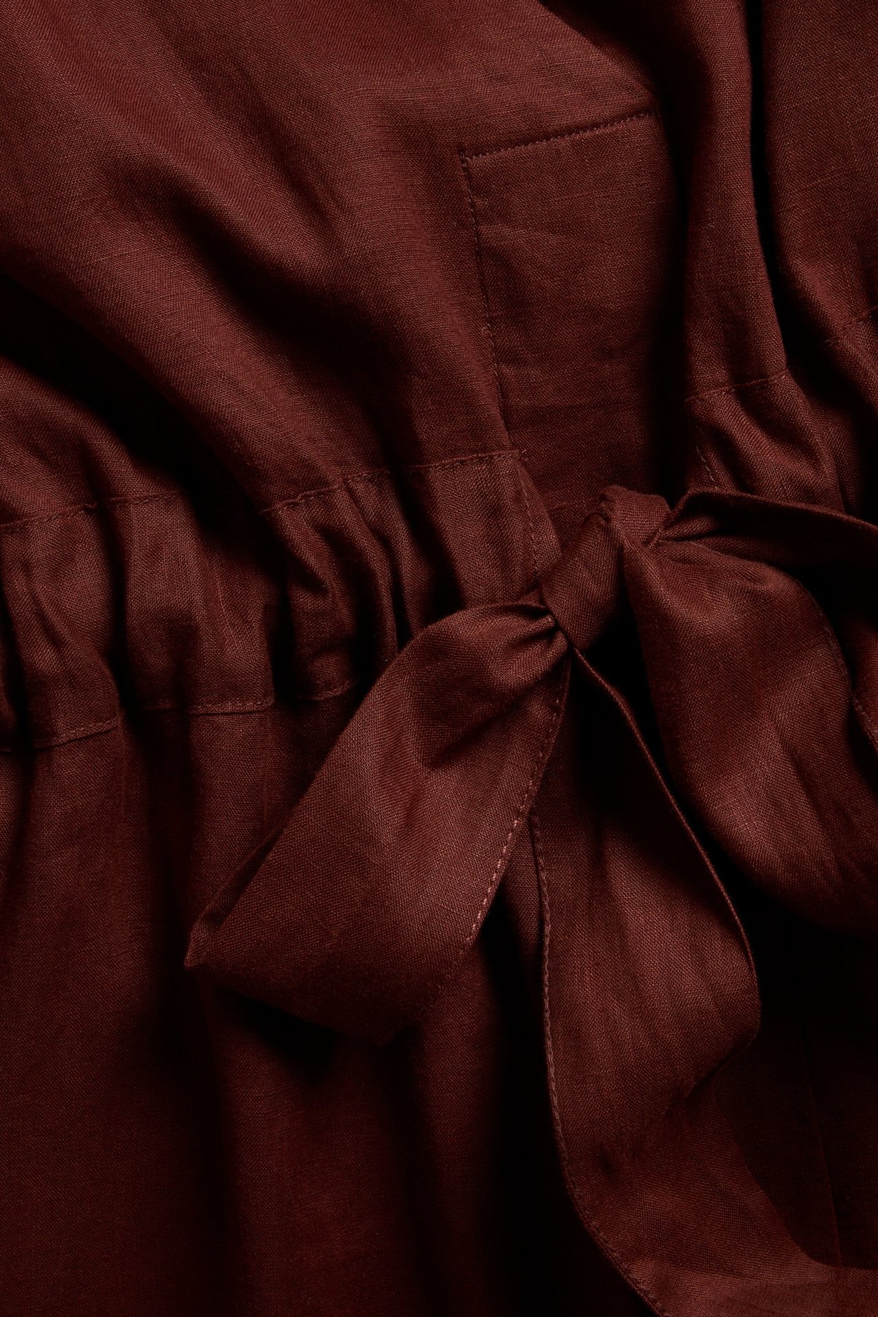 Närbild av en vinröd linneklänning med ett knutet tygbälte i midjan och en synlig sidoficka.