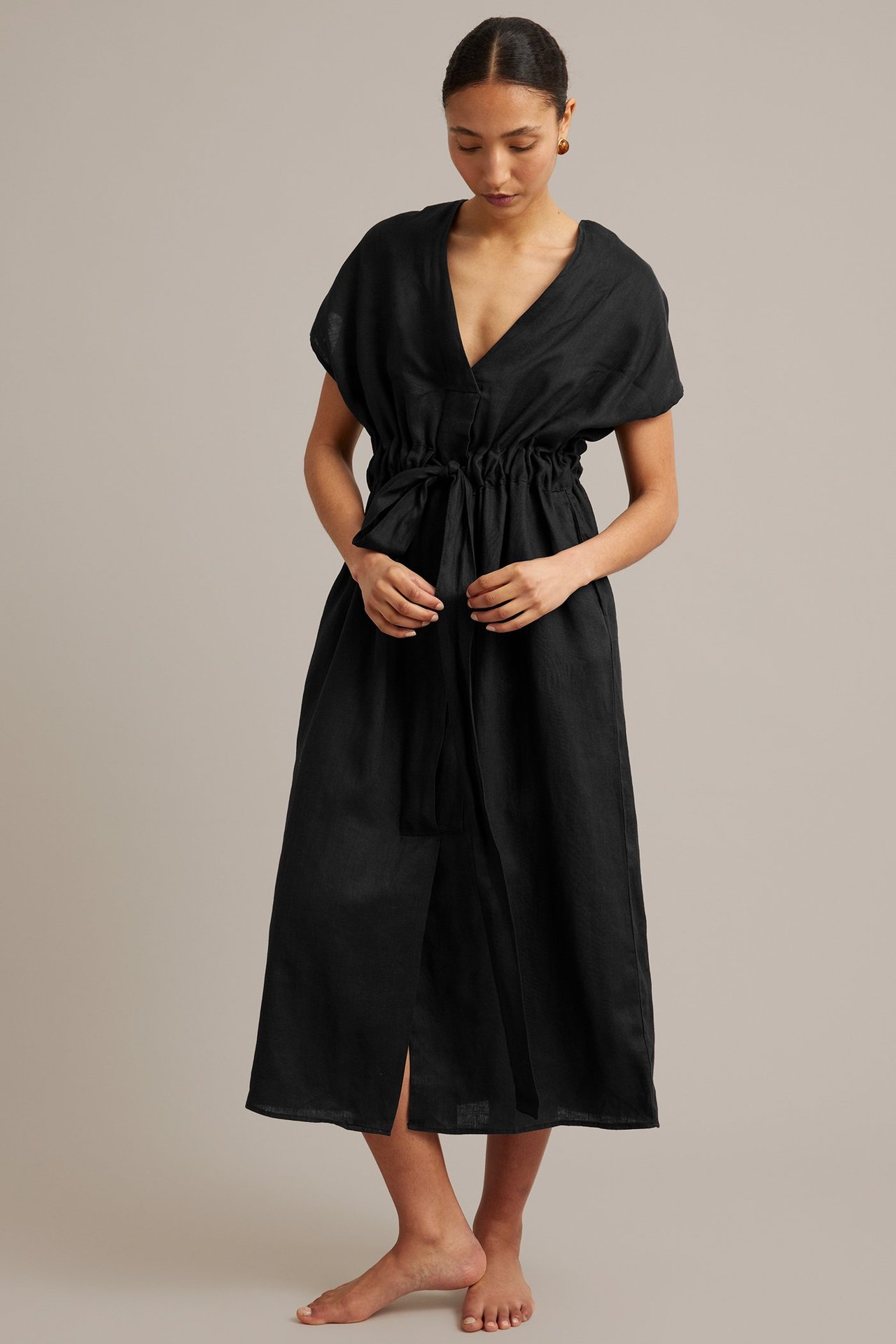 Frontvy av en kvinna i en svart linneklänning med V-ringning och knytband i midjan.