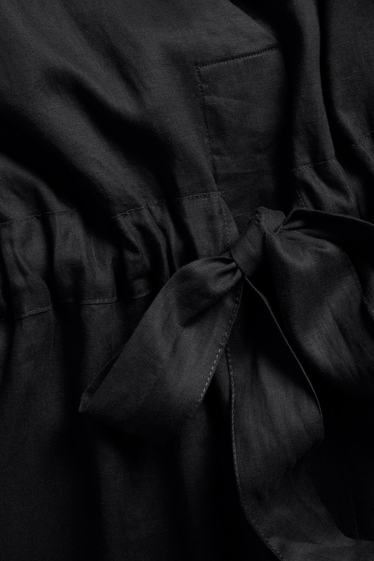 Närbild av en svart linneklänning med knytband i midjan och en synlig ficka.