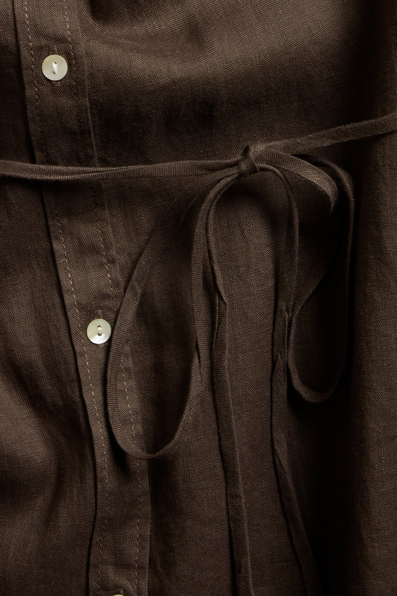 Lähikuva ruskeasta pellavapaidasta, jossa vaaleat napit ja solmittu vyötärönyöri.