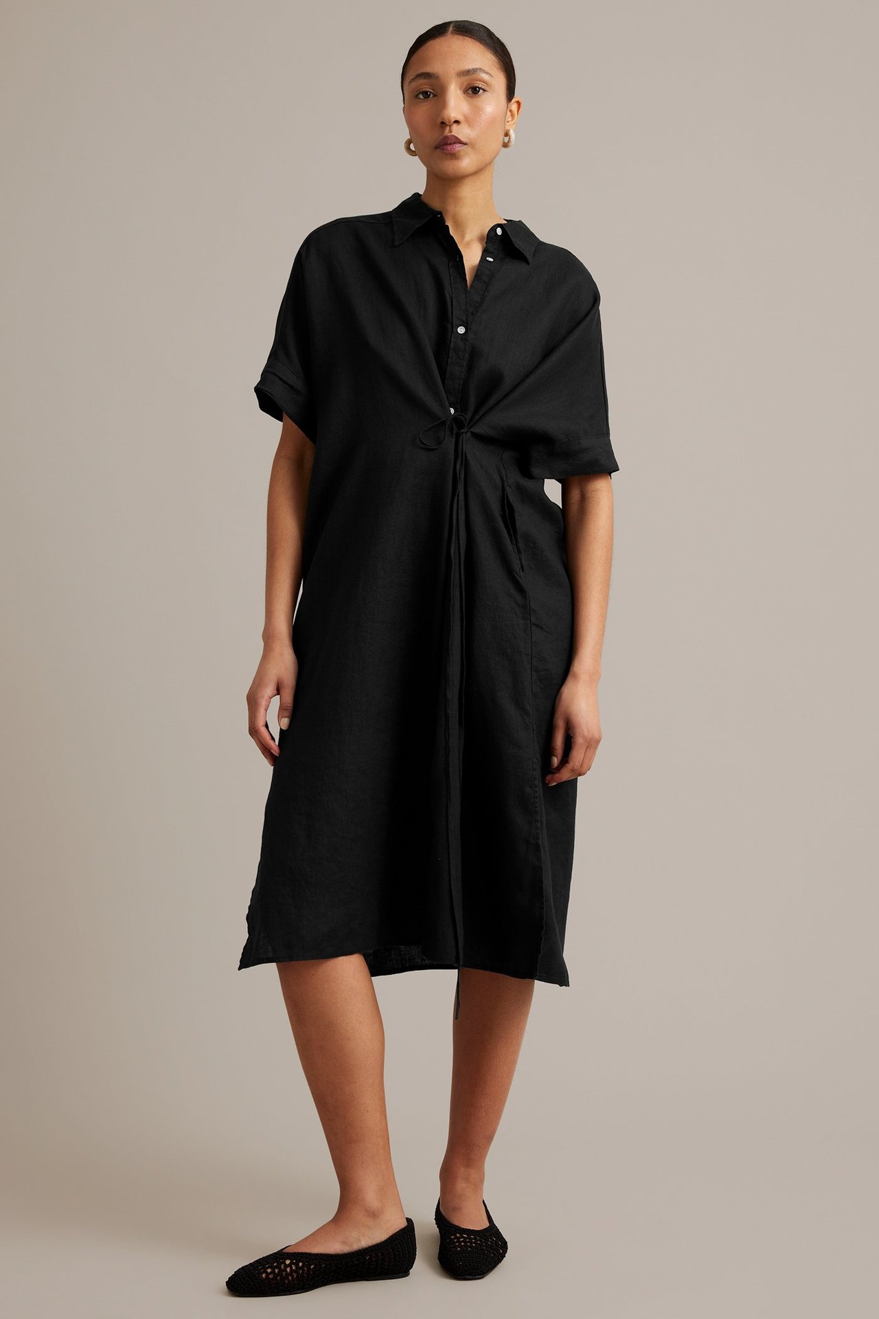 Forfra: kvinne i svart linskjortekjole med snøring i midjen og sorte vevde flate sko.