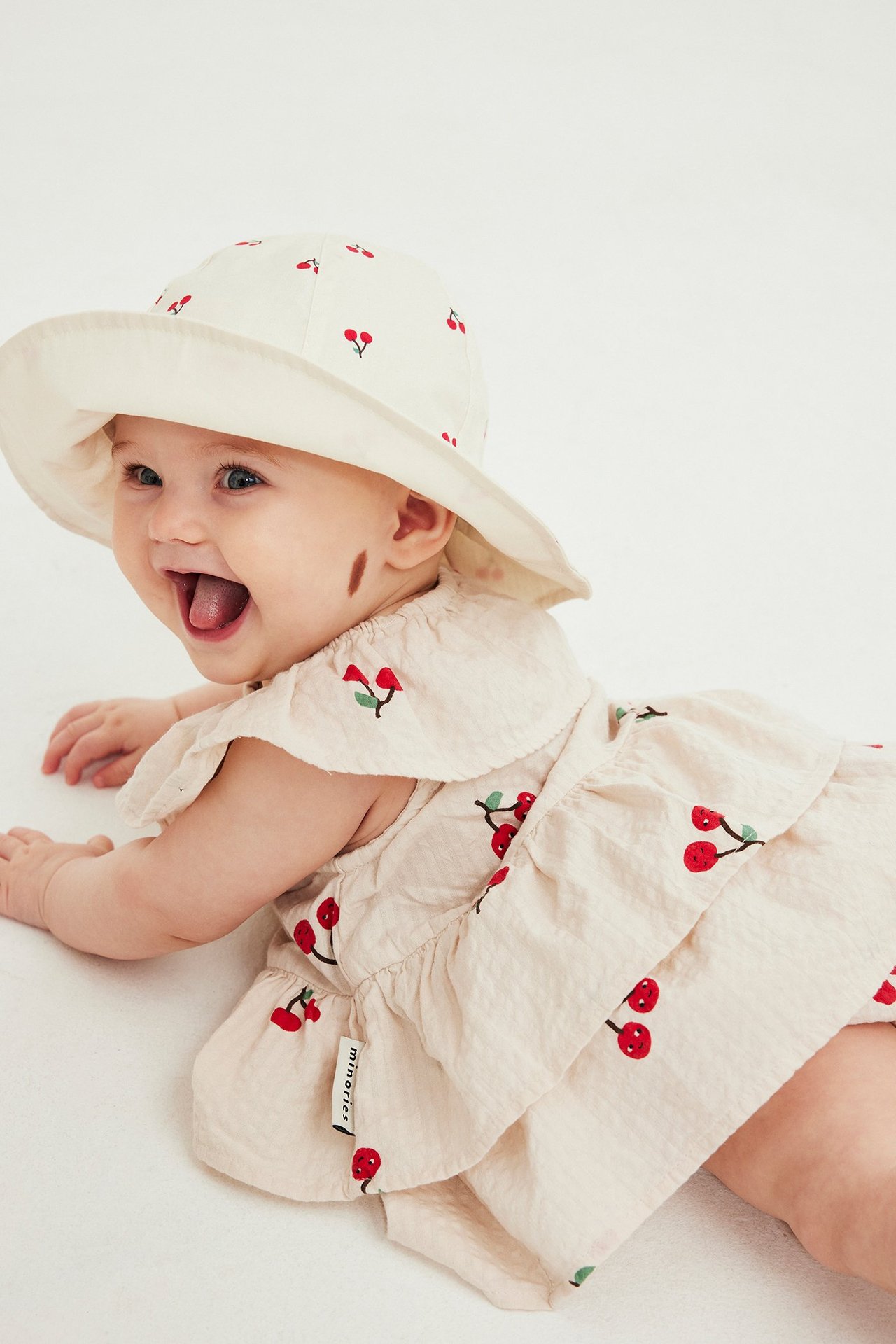 Widok z przodu: niemowlę w beżowej sukience w wiśnie z bloomersami i pasującym kapeluszem.
