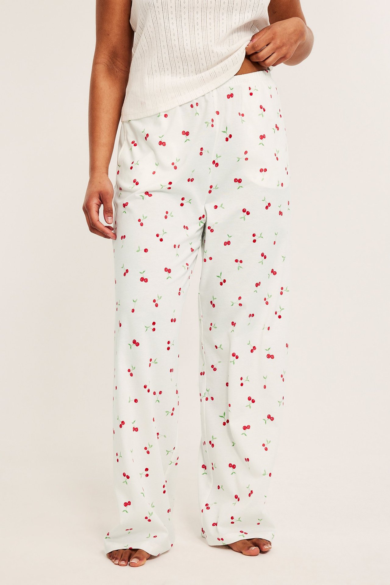 Edestäpäin nainen yllään luonnonvalkoiset puuvillapyjamahousut punaisella kirsikkakuviolla ja toppi.