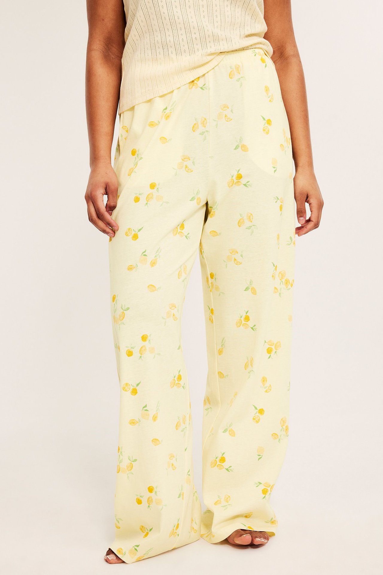 Naisen etukuva, yllään vaaleankeltaiset puuvillapyjamahousut hedelmäkuviolla ja neulottu toppi.