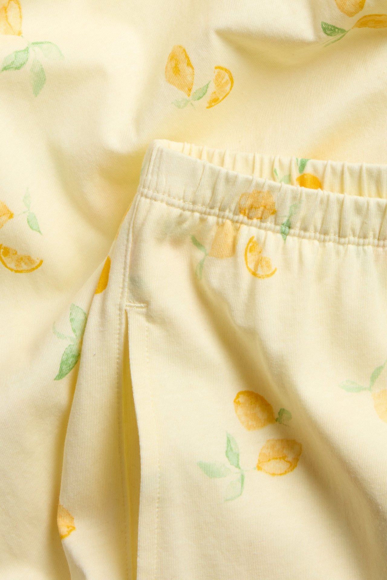 Lähikuva vaaleankeltaisista puuvillapyjamahousuista, joissa sitruunaprintti, joustava vyötärö ja sivutasku.