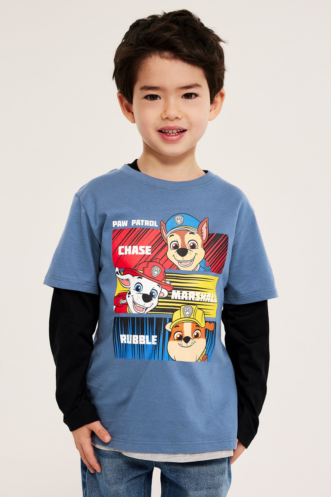 Widok z przodu: dziecko w niebieskim, bawełnianym T-shircie Paw Patrol, czarnej bluzce i niebieskich dżinsach.