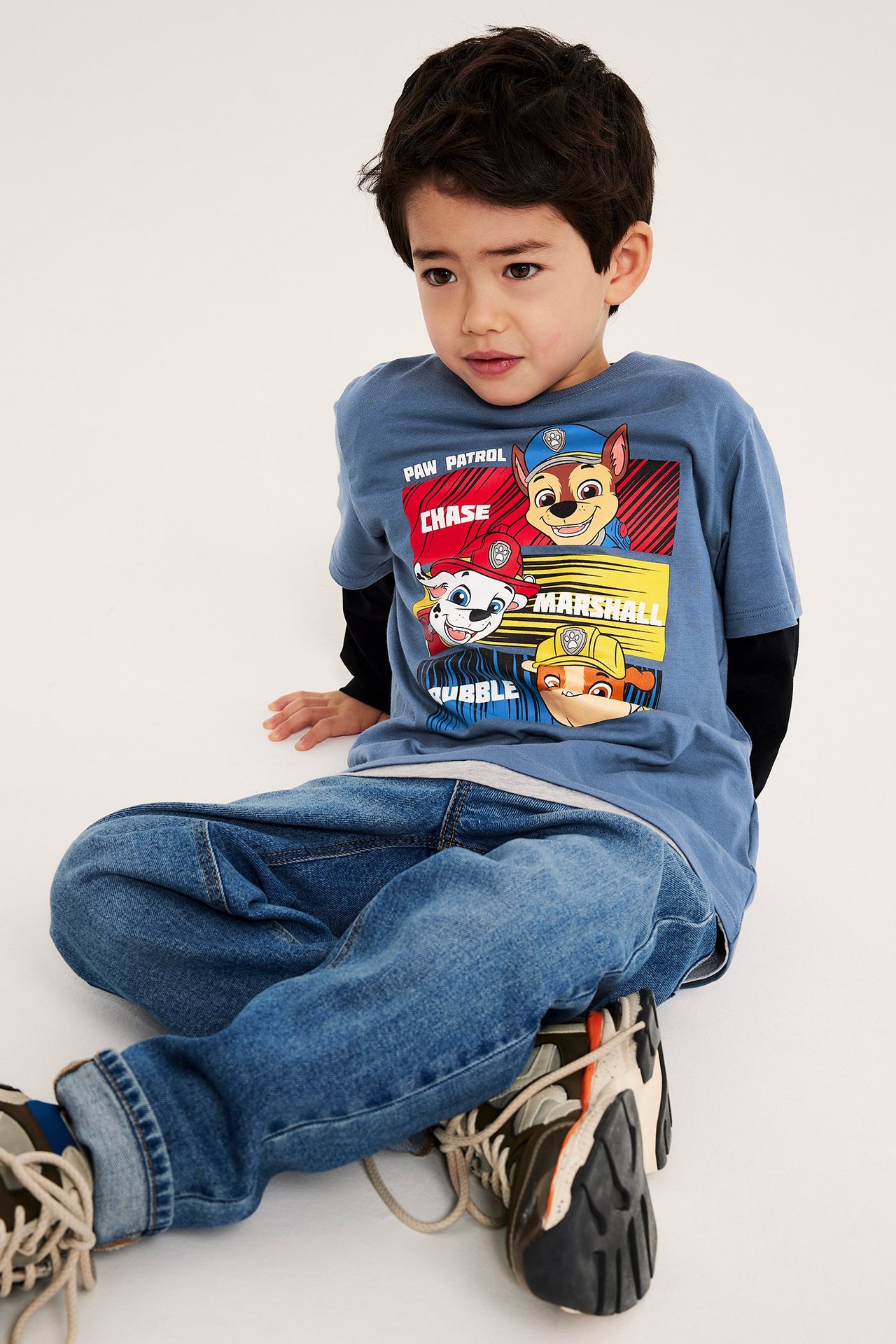 Widok z przodu: dziecko w niebieskiej koszulce Paw Patrol, czarny longsleeve, niebieskie dżinsy, sneakersy.