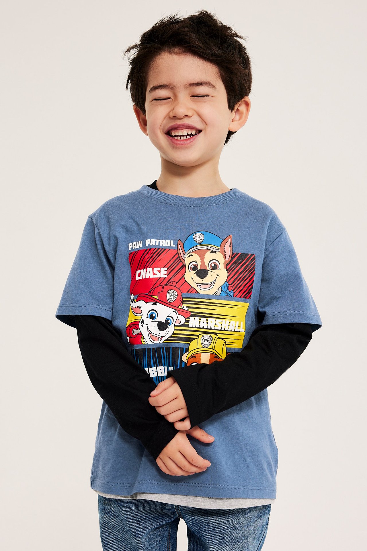 Lapsen sininen Ryhmä Hau -printtipaita mustan pitkähihaisen paidan päällä, sinisten farkkujen kanssa. Edestä.