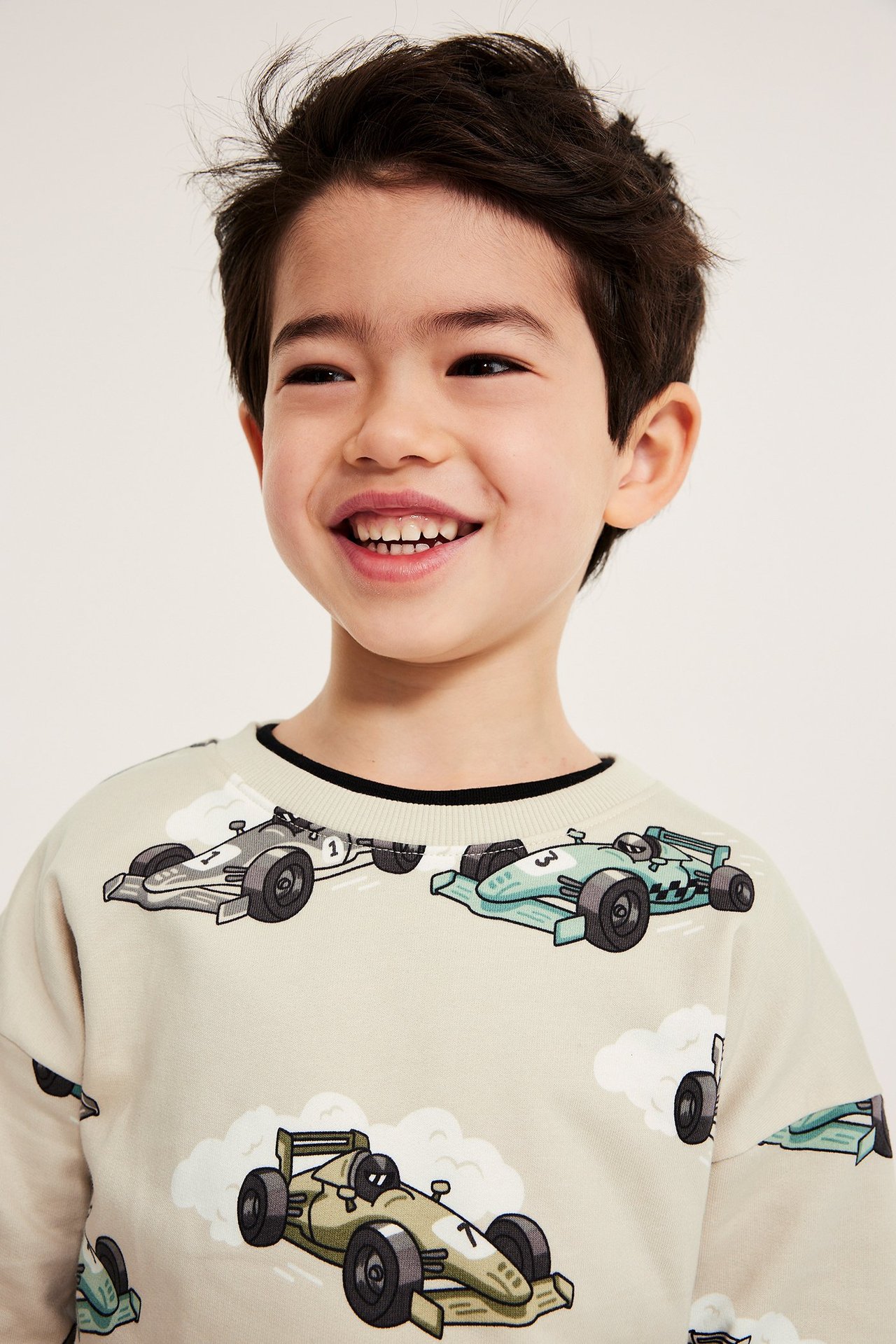 Närbild framifrån på ett leende barn i en beige sweatshirt med heltäckande biltryck.