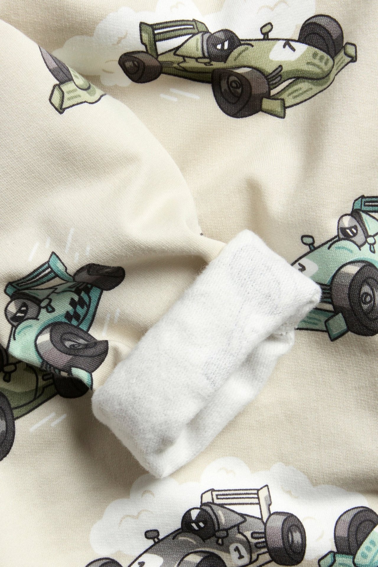 Närbild på en beige sweatshirt för barn med heltäckande bilmönster och vit ribbad mudd.