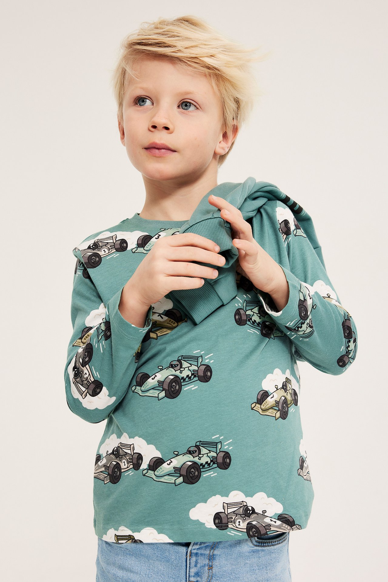 Forfra: Barn bærer en lysegrønn langermet t-skjorte i bomull med bilprint og blå jeans.