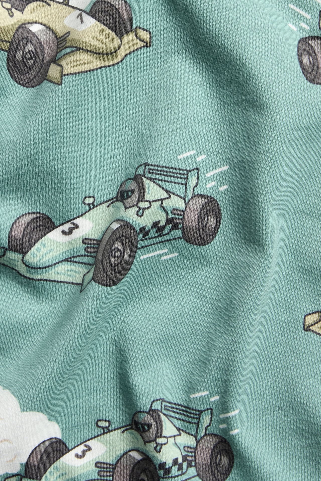 Nærbilde av en lysegrønn langermet t-skjorte i bomull med heldekkende mønster av racerbiler.