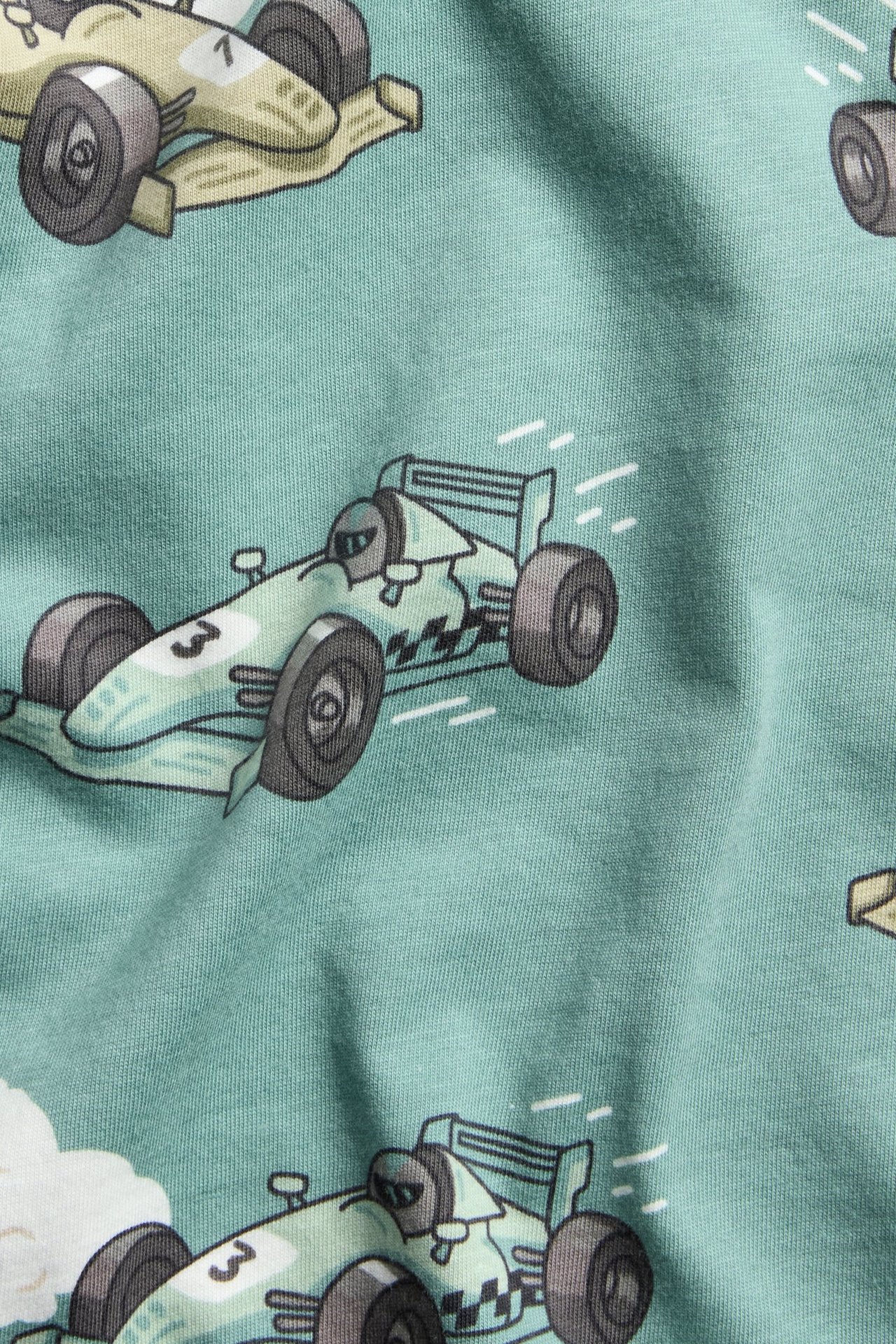 Zbliżenie na jasnozieloną, bawełnianą koszulkę z długim rękawem z nadrukiem wyścigowych samochodów.