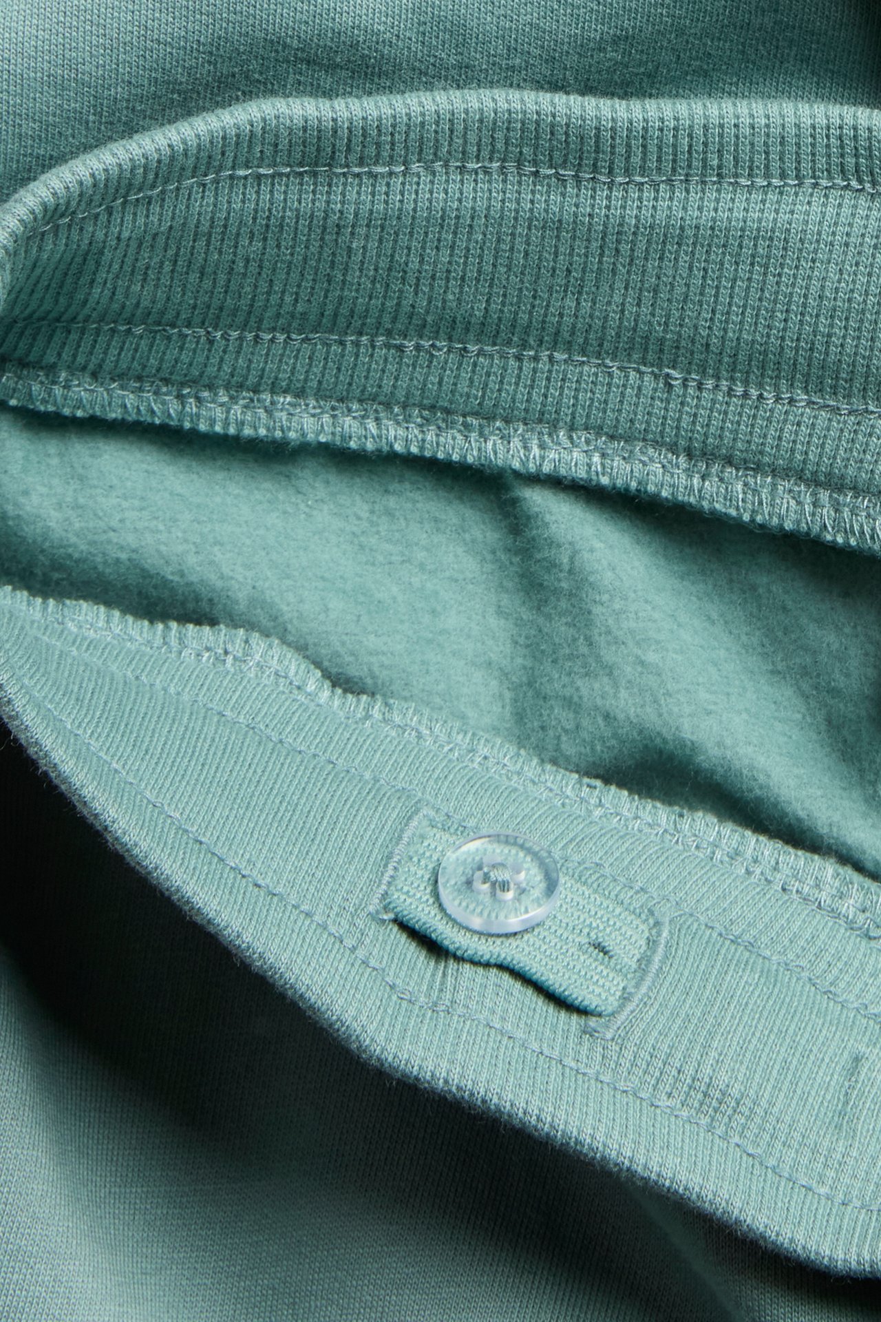 Nærbilde av lysegrønne bomullsjoggebukser, viser ribbestrikket justerbar midje og myk innside med knapp.