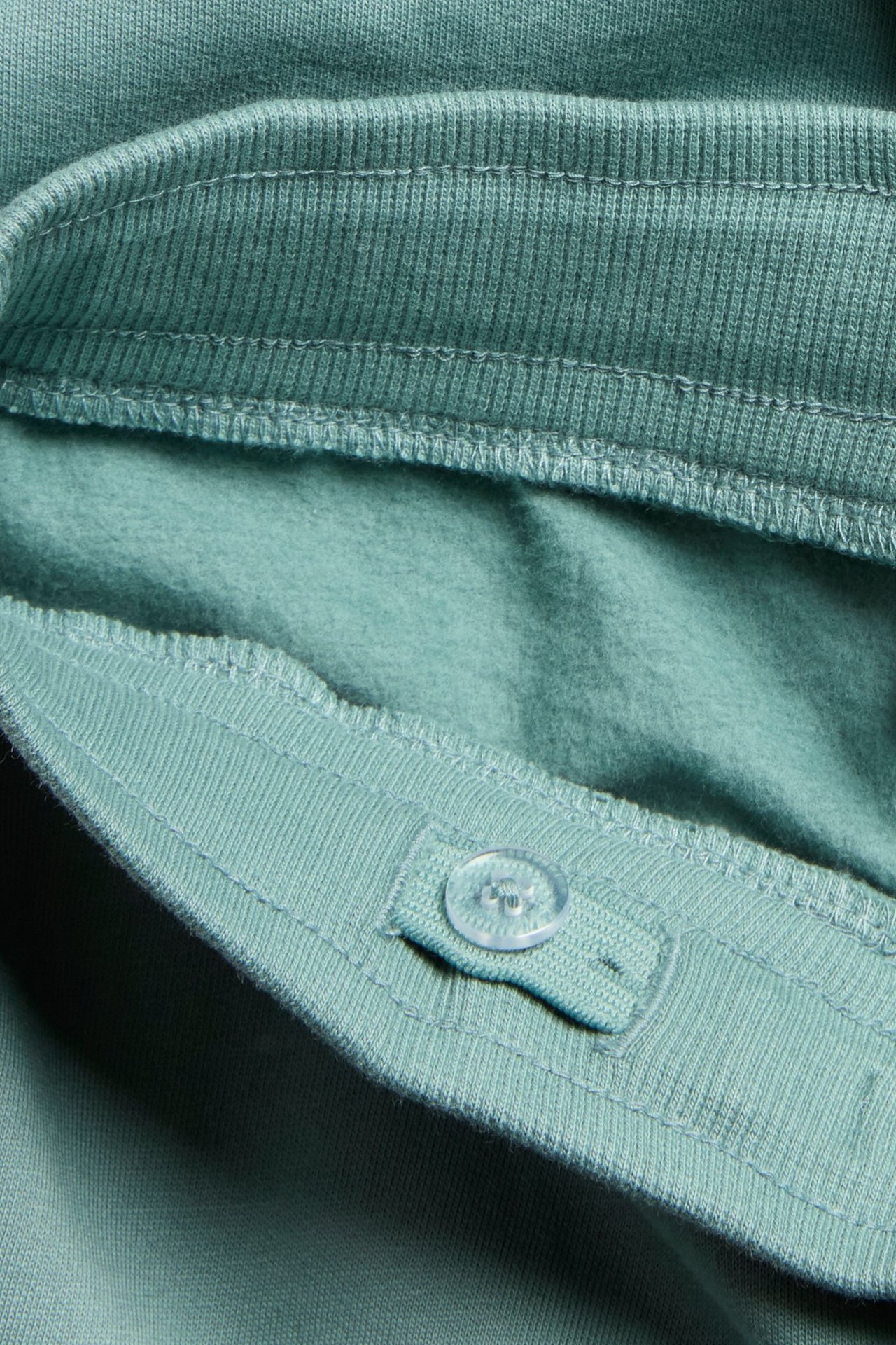 Zbliżenie na jasnozielone bawełniane spodnie dresowe, widać prążkowany regulowany pas i miękką podszewkę z guzikiem.