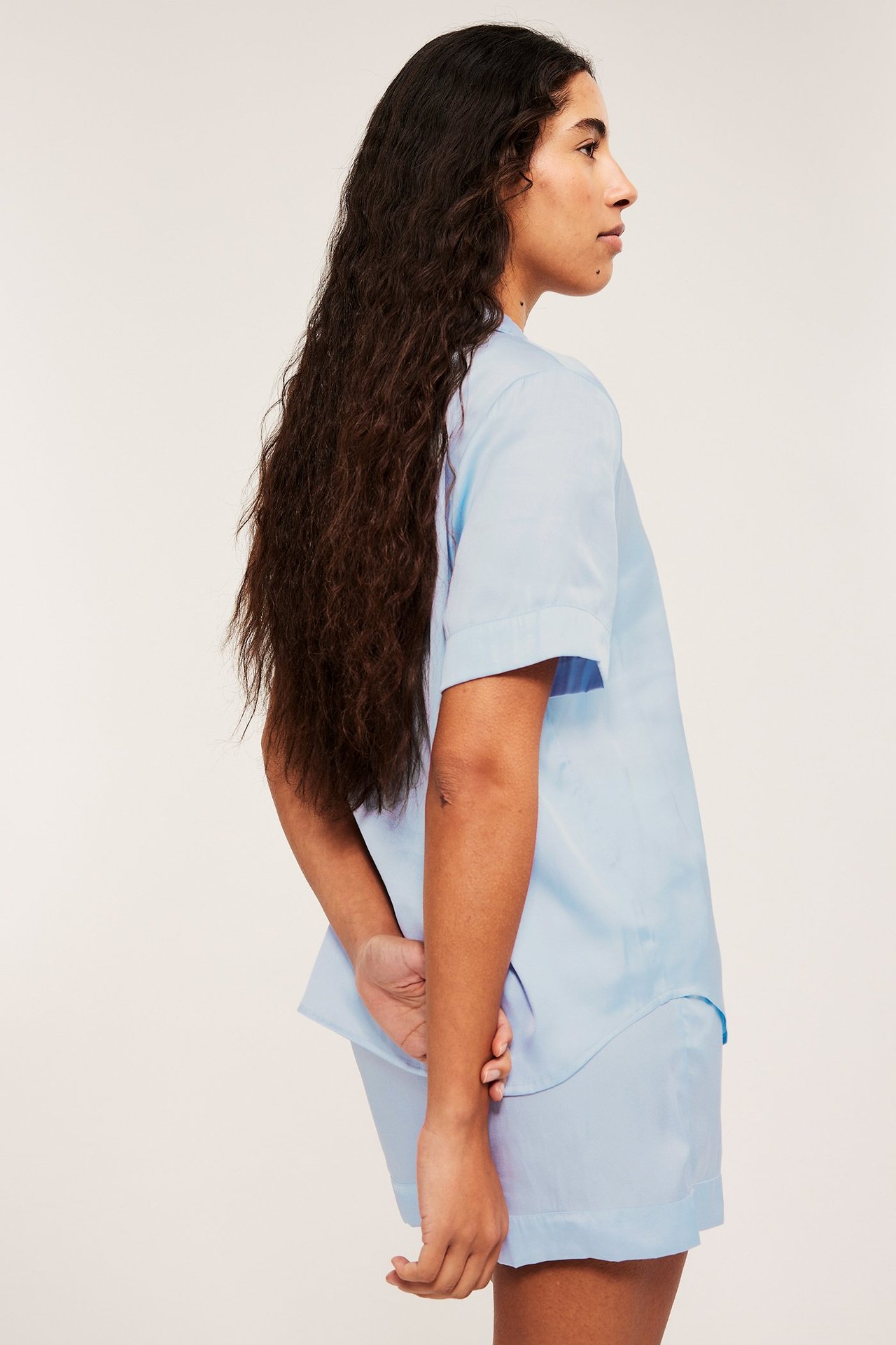 Sidebilde av en kvinne i lyseblått viskosesatin-pysjamas-sett med kortarmet topp og shorts.