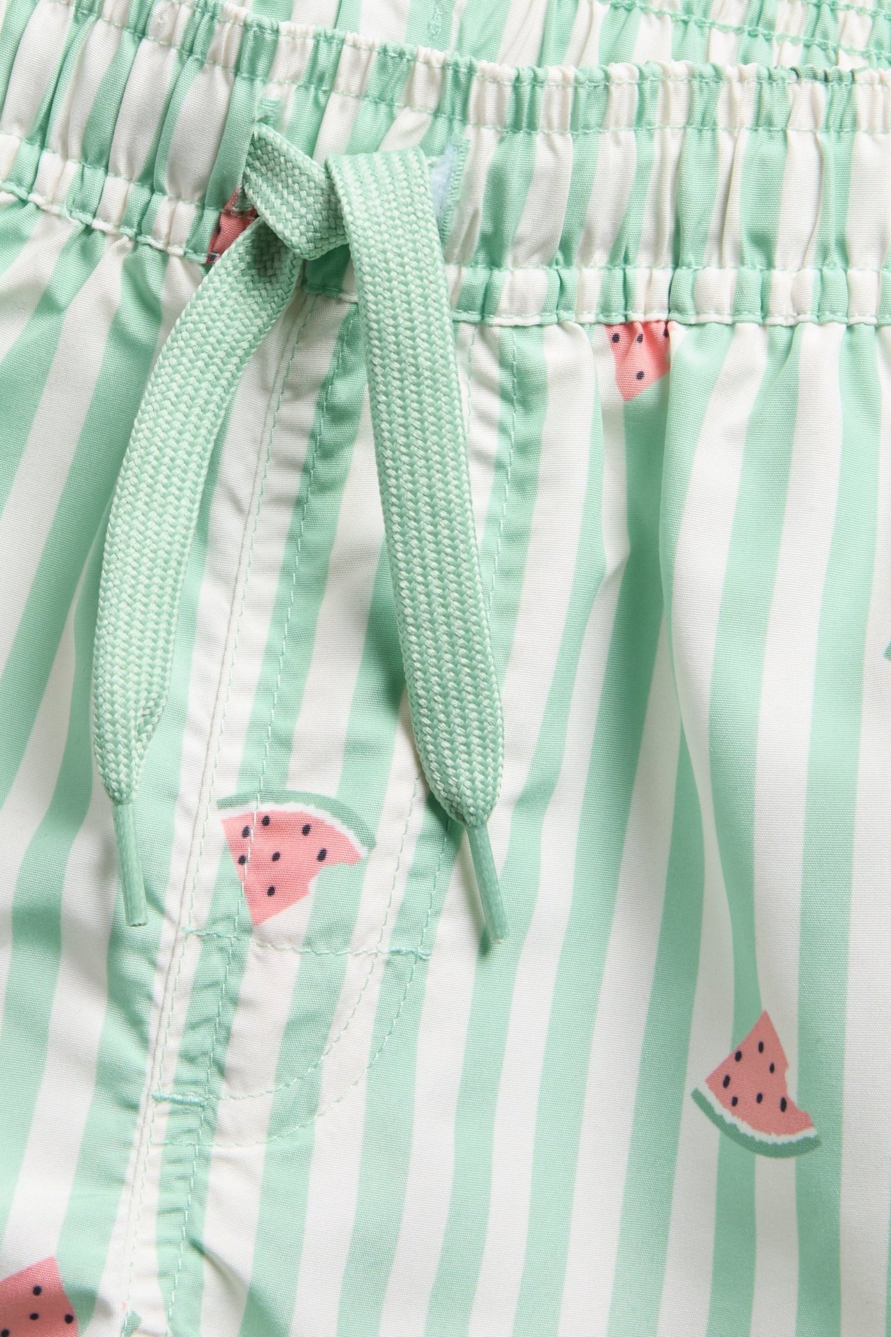 Zbliżenie dziecięcych zielono-białych szortów kąpielowych w paski, z wzorem arbuza i sznurkiem.
