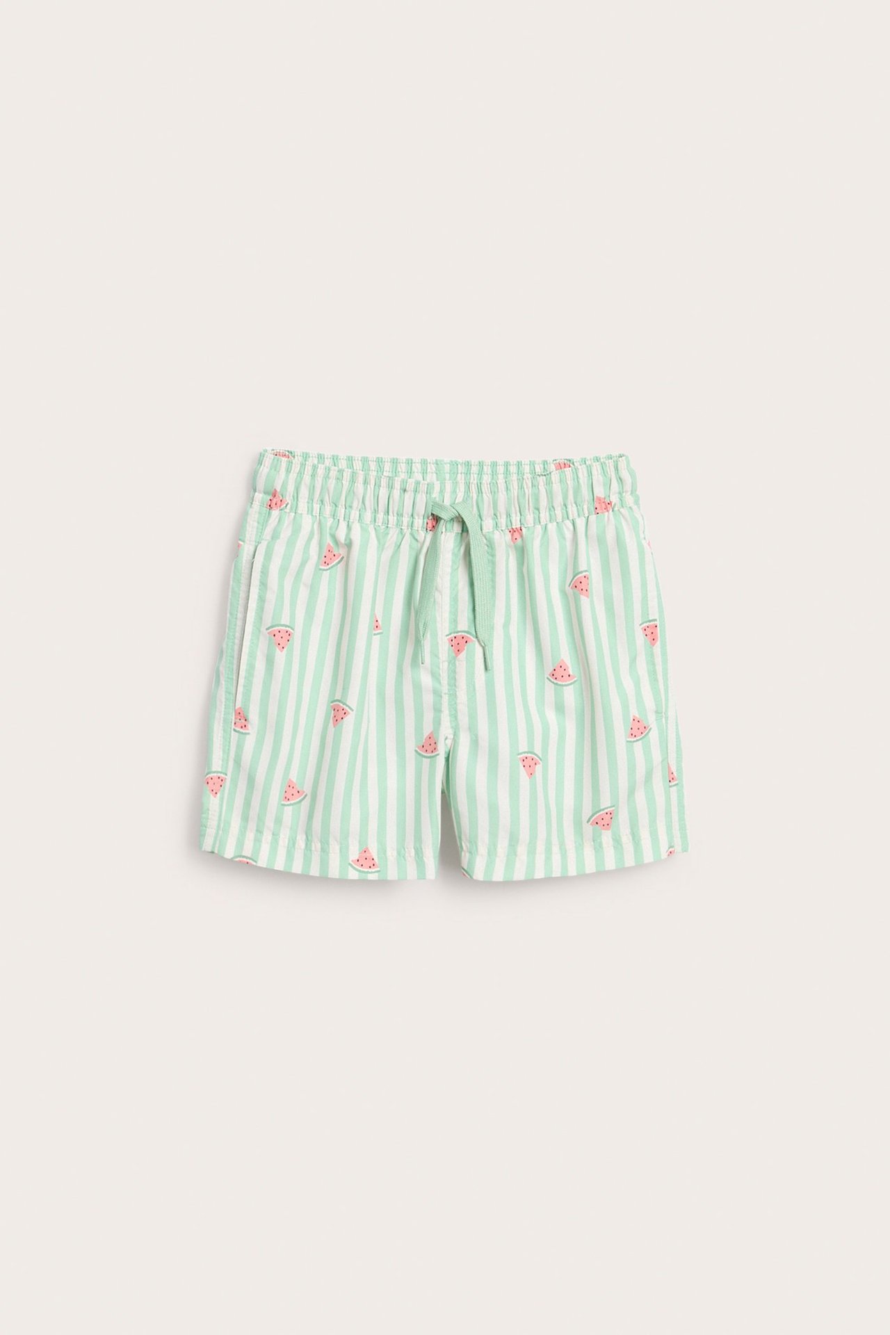 Frontvisning av grønne og hvite stripete badeshorts for barn, med vannmelonmønster og snøring i livet.