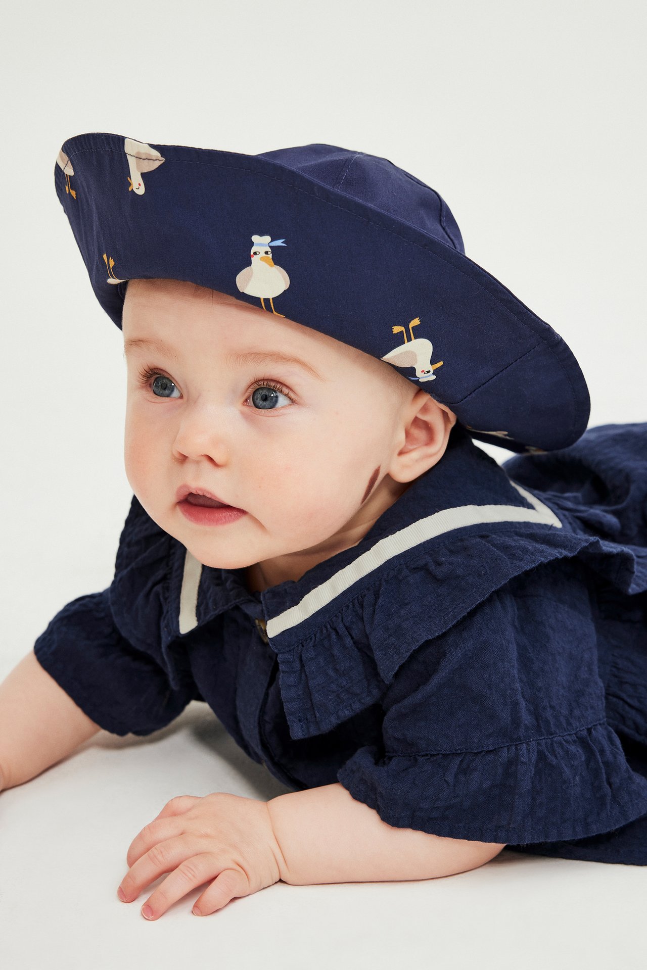 Nærbilde av baby i mørkeblå hatt med måkemønster og mørkeblå rysjet seersucker-kjole.