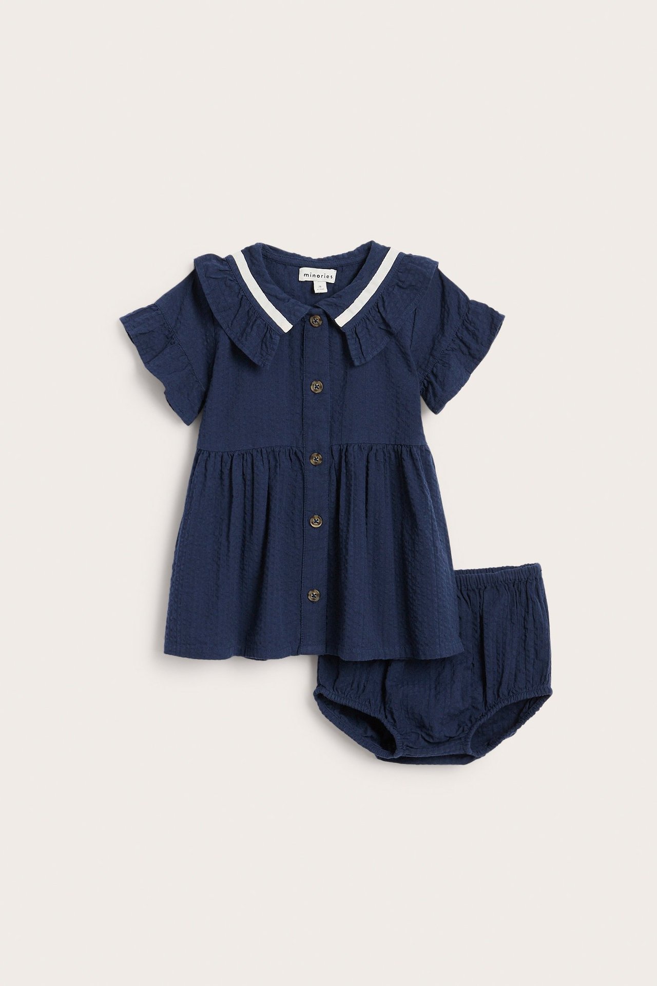 Frontvisning av en blå seersucker babykjole med hvitstripet volangkrave, korte ermer og matchende bloomers.