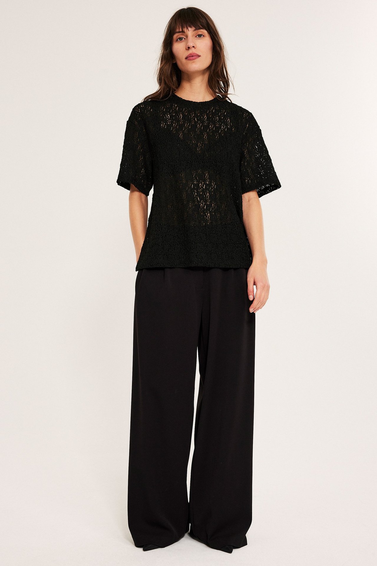 Kvinne i svart blonde loose topp og vide svarte bukser, front.