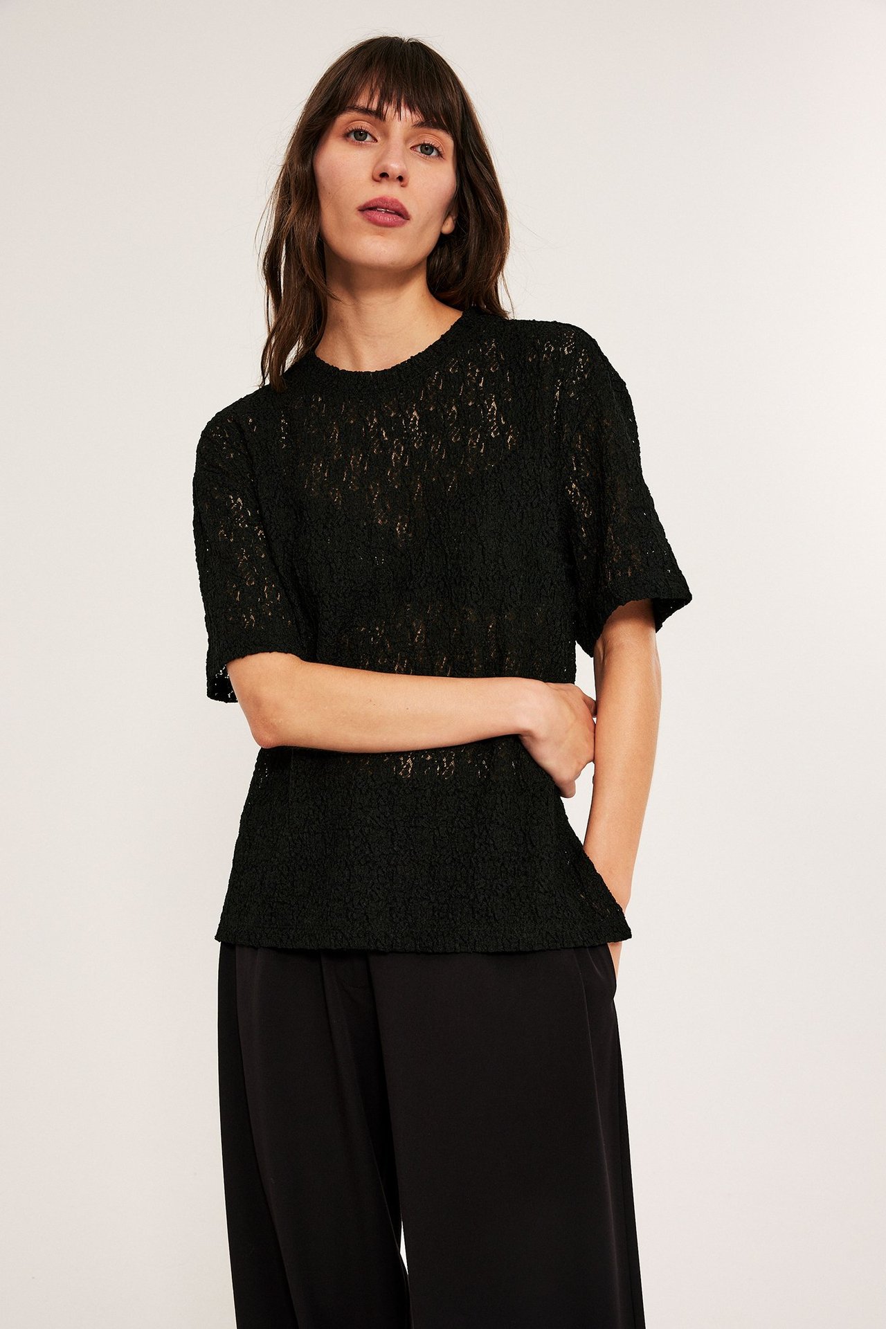 Kvinne i svart blond liten topp med kort erme, over svarte bukser, front.