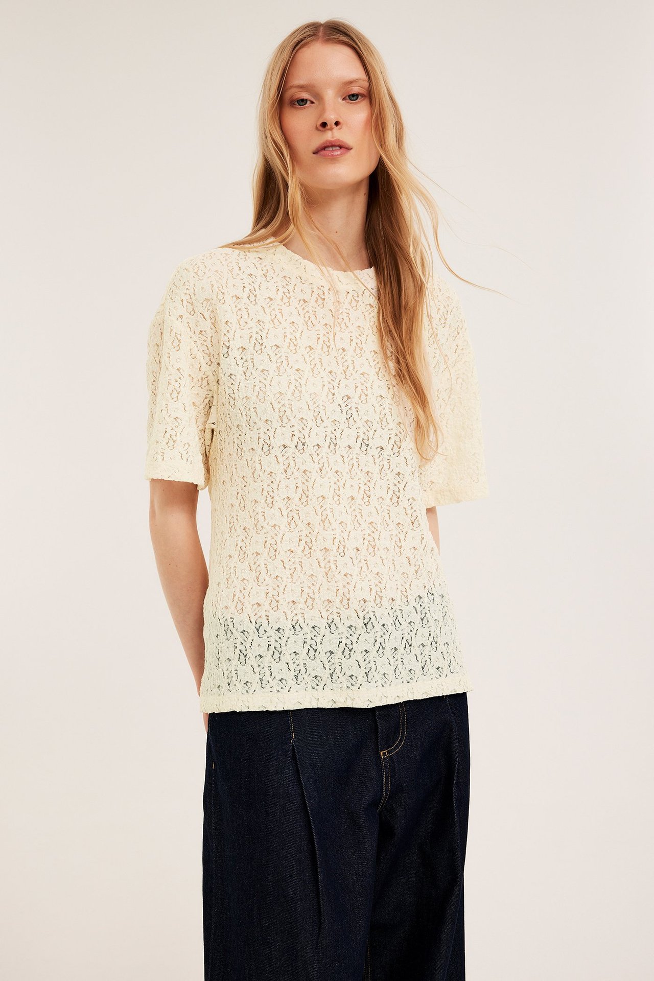 Framifrån, en kvinna i en lös offwhite kortärmad spetstopp och mörkblå vida byxor.