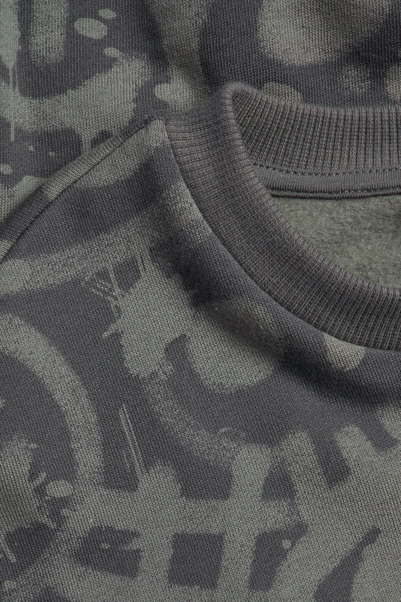 Zbliżenie szarej bluzy z mieszanki bawełny z abstrakcyjnym wzorem i prążkowanym okrągłym dekoltem.