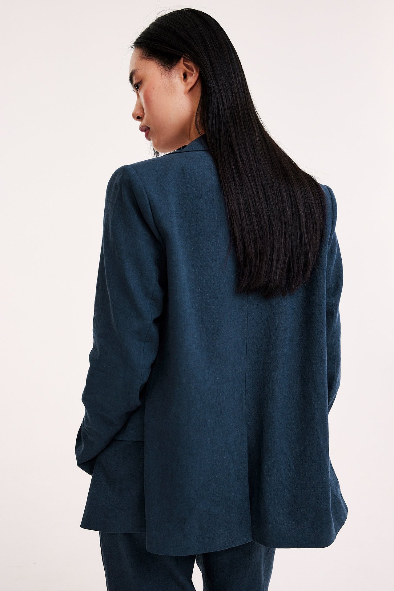 Widok z tyłu kobiety w granatowej melanżowej marynarce z lnu i pasujących spodniach.
