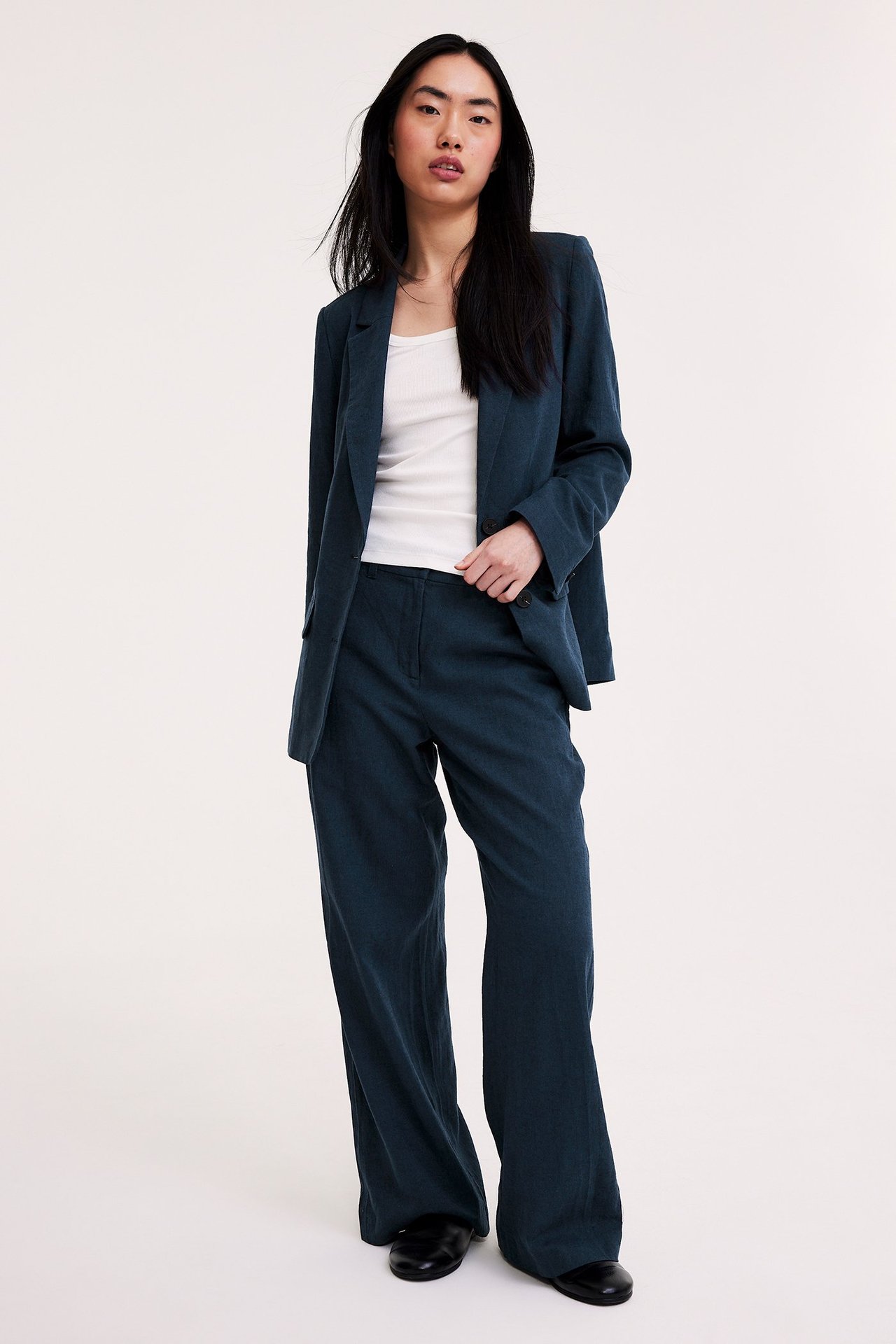 Edestä: nainen tummansinisessä avonaisessa melange pellavasekoitebleiserissä, valkoisessa topissa ja leveissä housuissa.