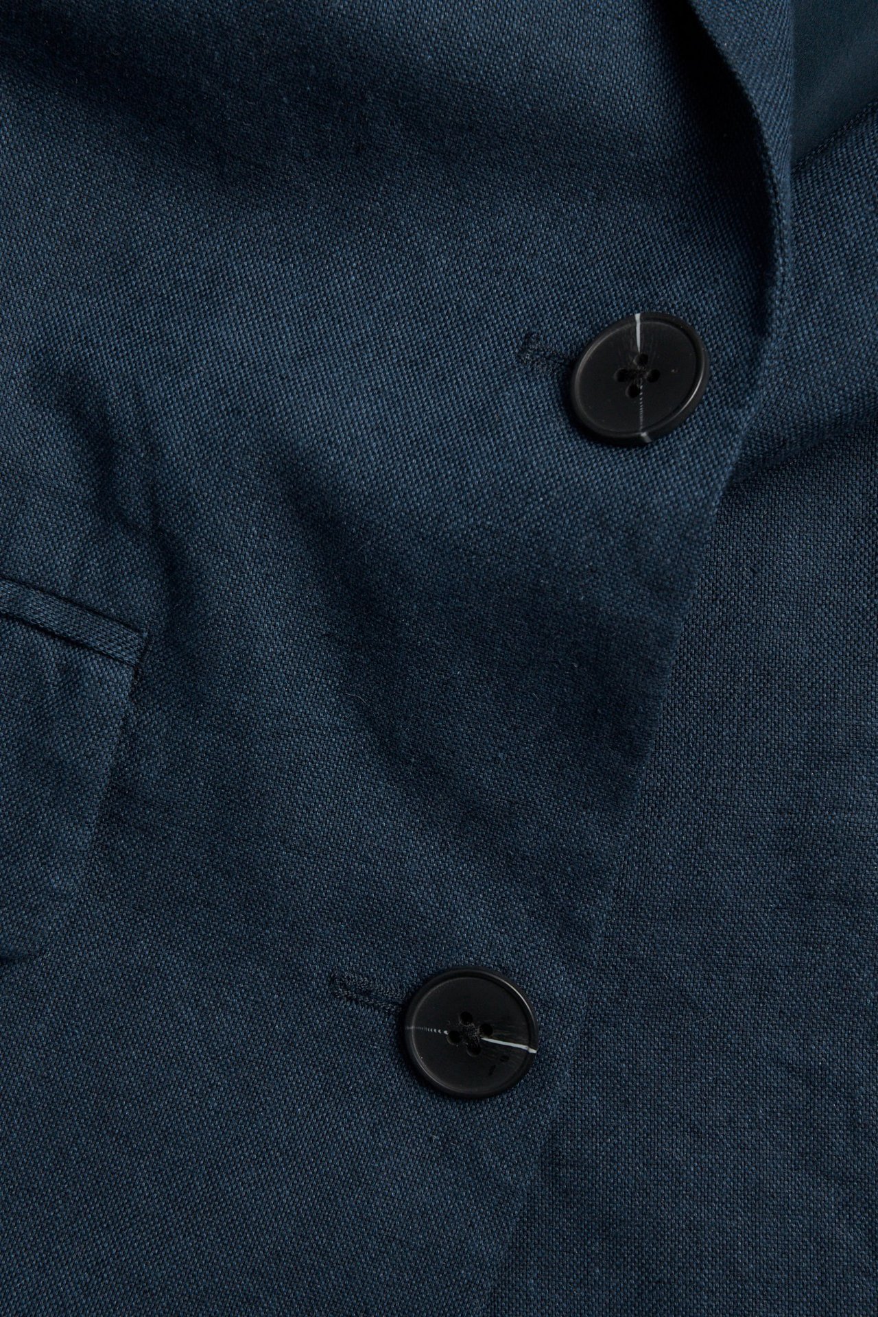Zbliżenie na granatową marynarkę z mieszanki lnu, z dwoma czarnymi guzikami i kieszenią z patką.