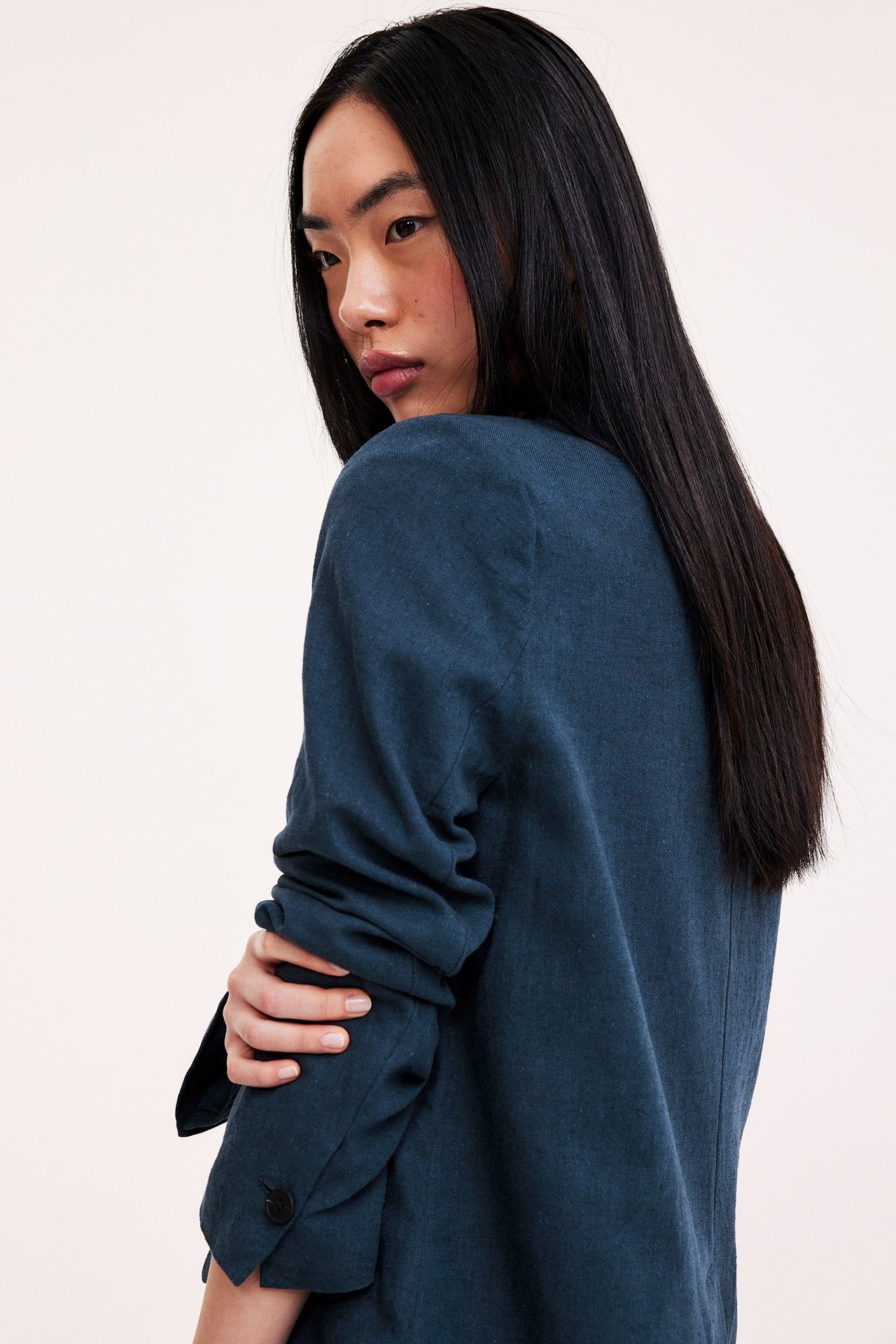 Nainen yllään tummansininen meleerattu pellavasekoitekavaj, takaapäin. Hihansuu nappiyksityiskohdalla.