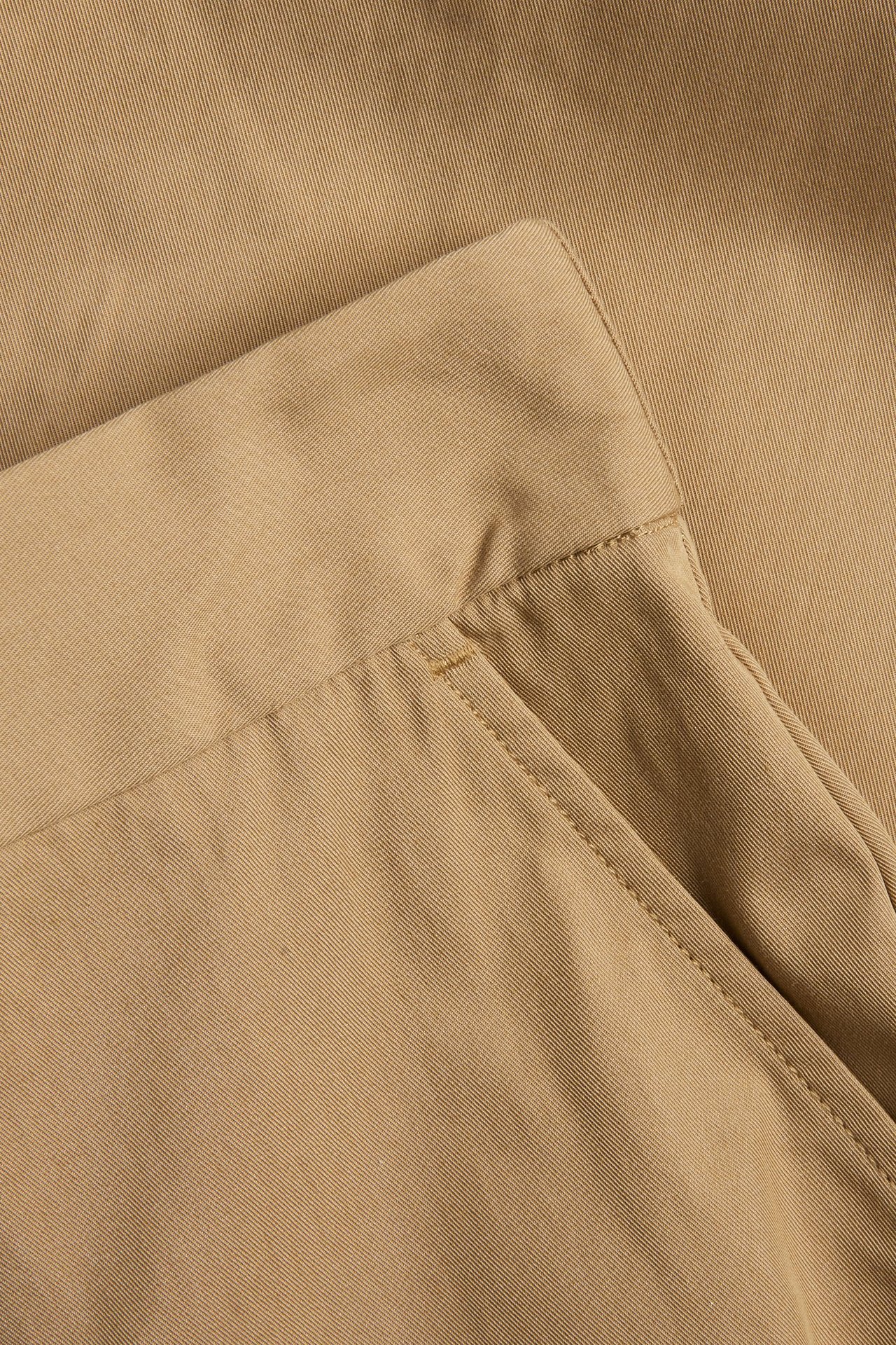 Nærbilde av beige bomullsblandede Bermudashorts som viser stoffstruktur og en lommeåpning.